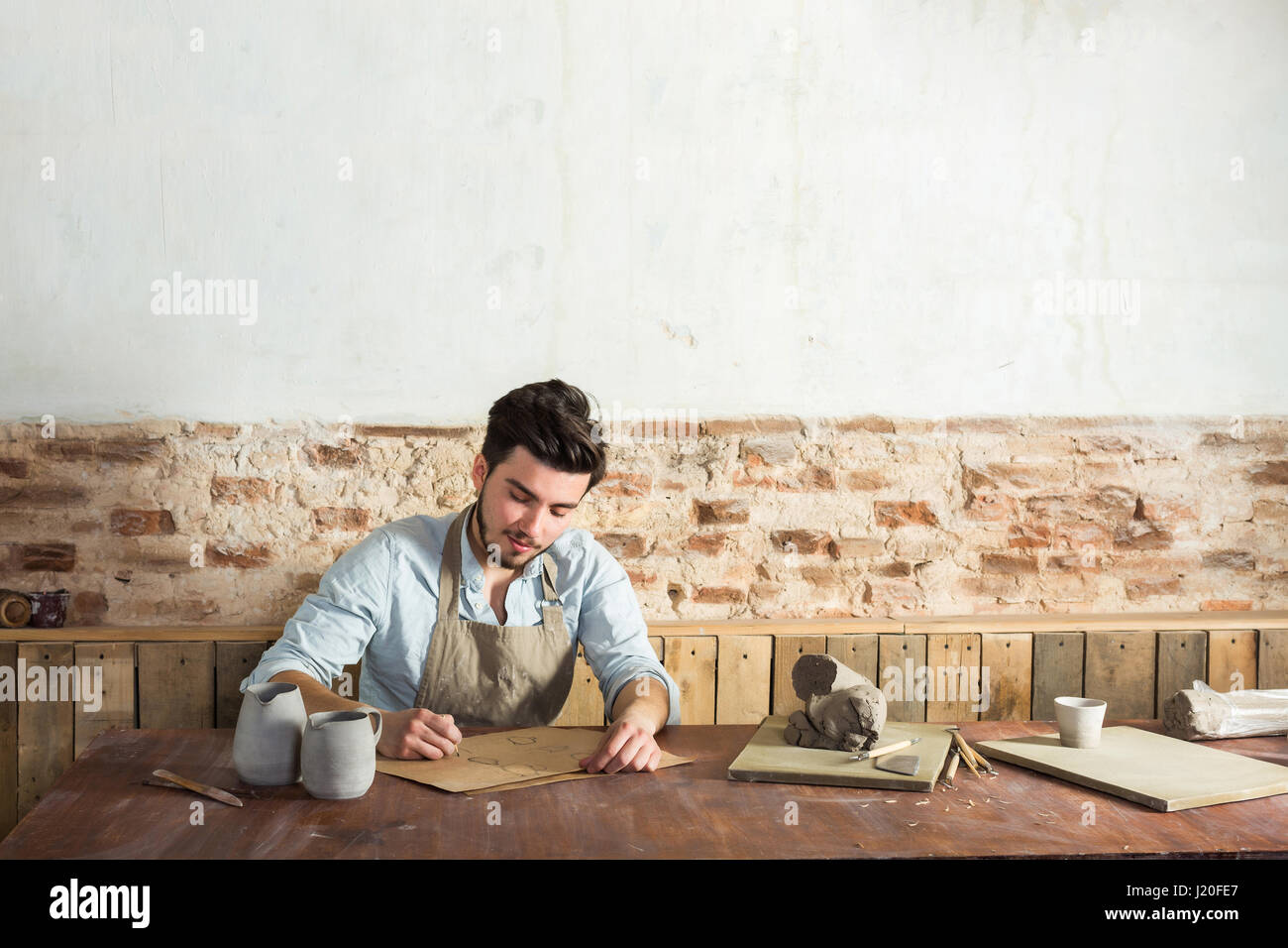 the smiling handsome young mexican potter does sketches of ceramics on the paper. concept of small business, handcrafted work. picture with empty space for the text. Stock Photo