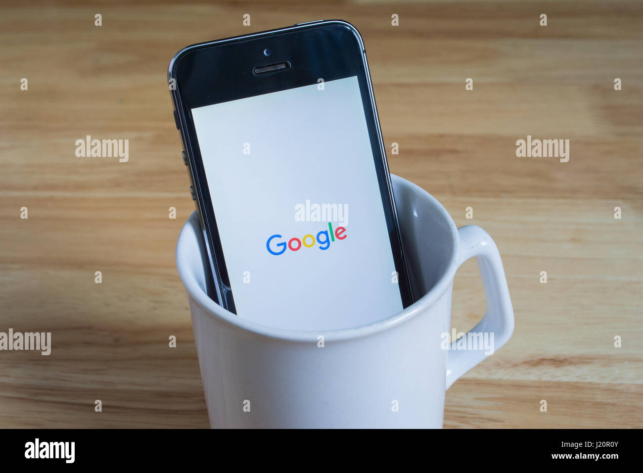 Bangkok, Thailand - April 22, 2017 : Apple iPhone5s in a mug showing its screen with Google logo. Stock Photo