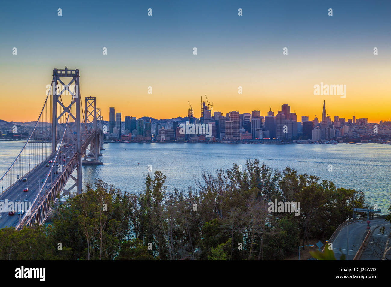 Classic panoramic view of famous Oakland Bay Bridge with the skyline of San Francisco illuminated in beautiful twilight with sunset glow in summer, Ca Stock Photo
