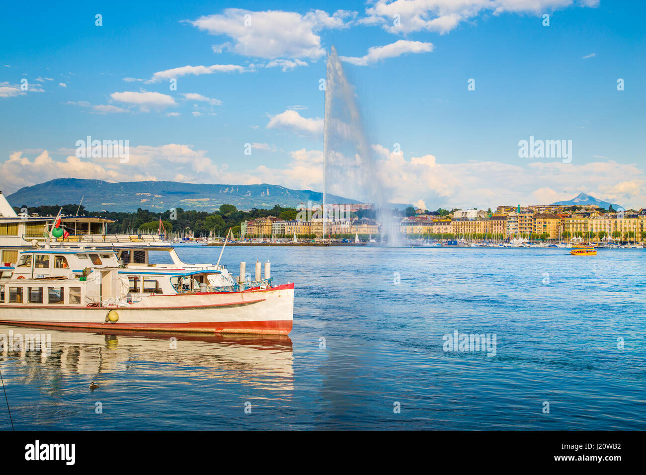 Panorama view of historic Geneva skyline with famous Jet d'Eau fountain and ships at harbor district in beautiful evening light at sunset, Switzerland Stock Photo