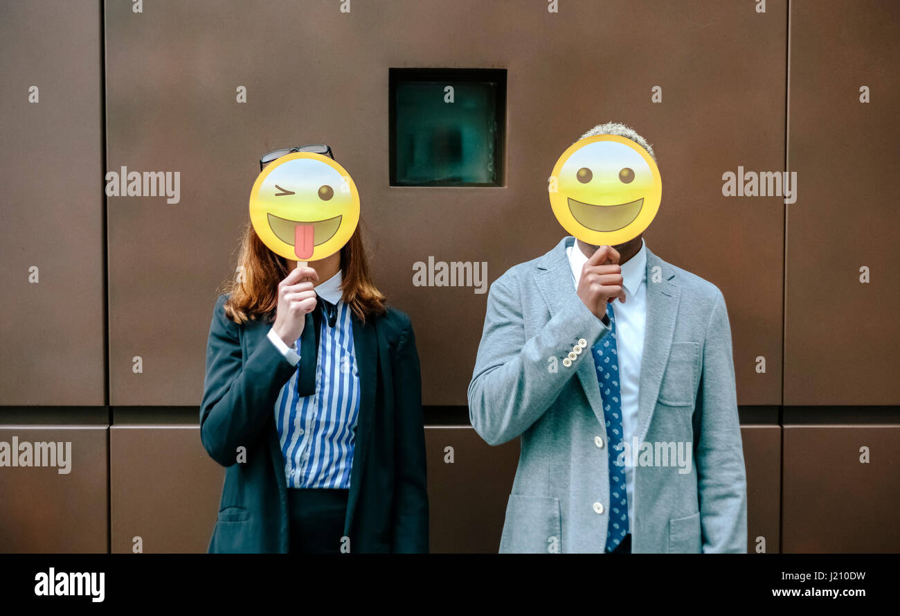 Young businessman and woman covering faces with emoji masks Stock Photo