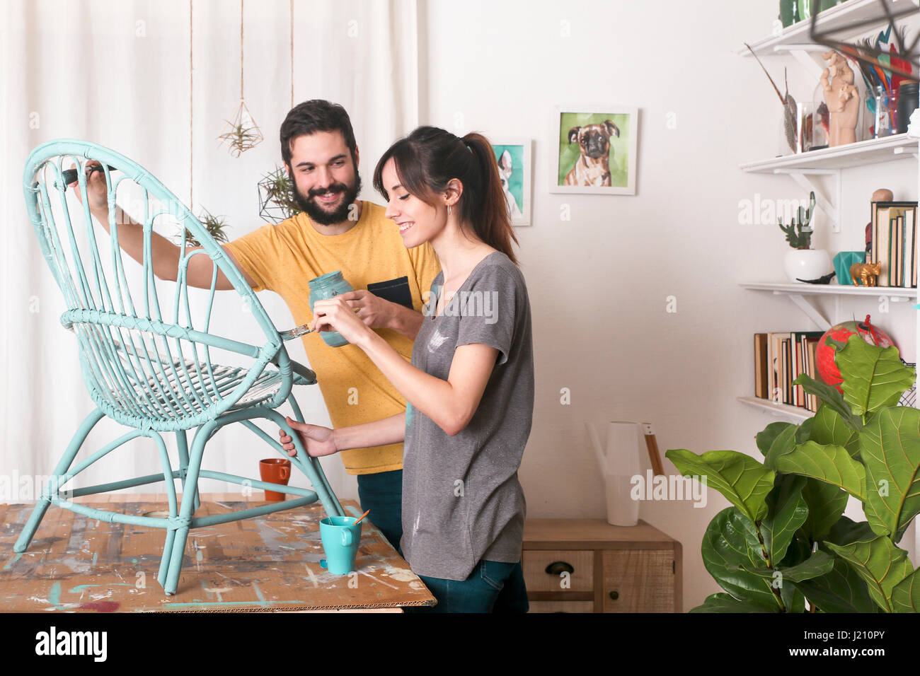 Young couple painting wicker armchair in blue at home Stock Photo