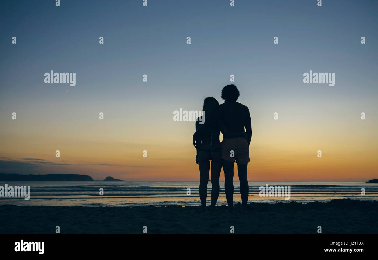Young couple watching the sunset on the beach Stock Photo - Alamy