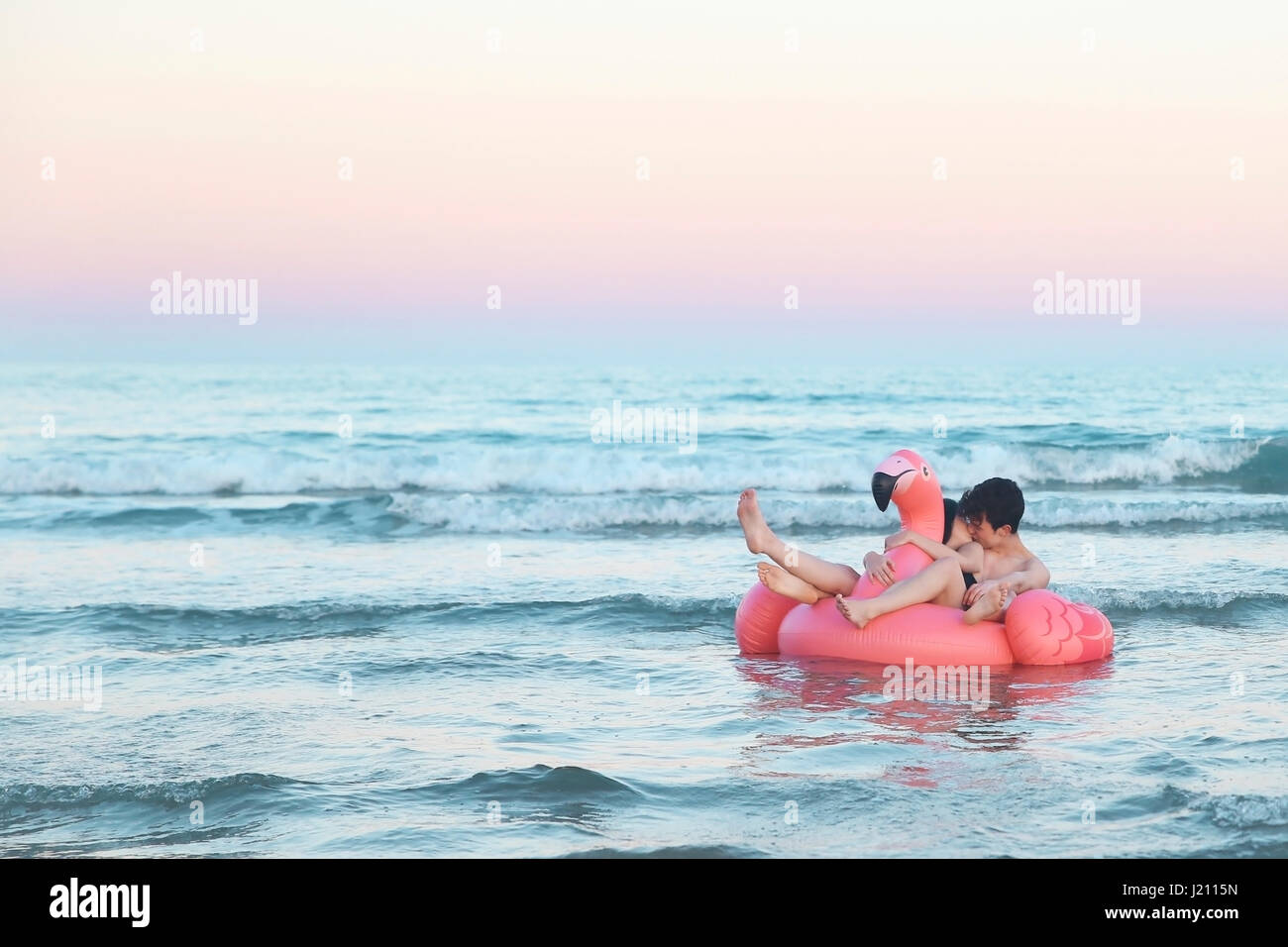 Couple in love floating with inflatable pink flamingo on the sea at sunset Stock Photo
