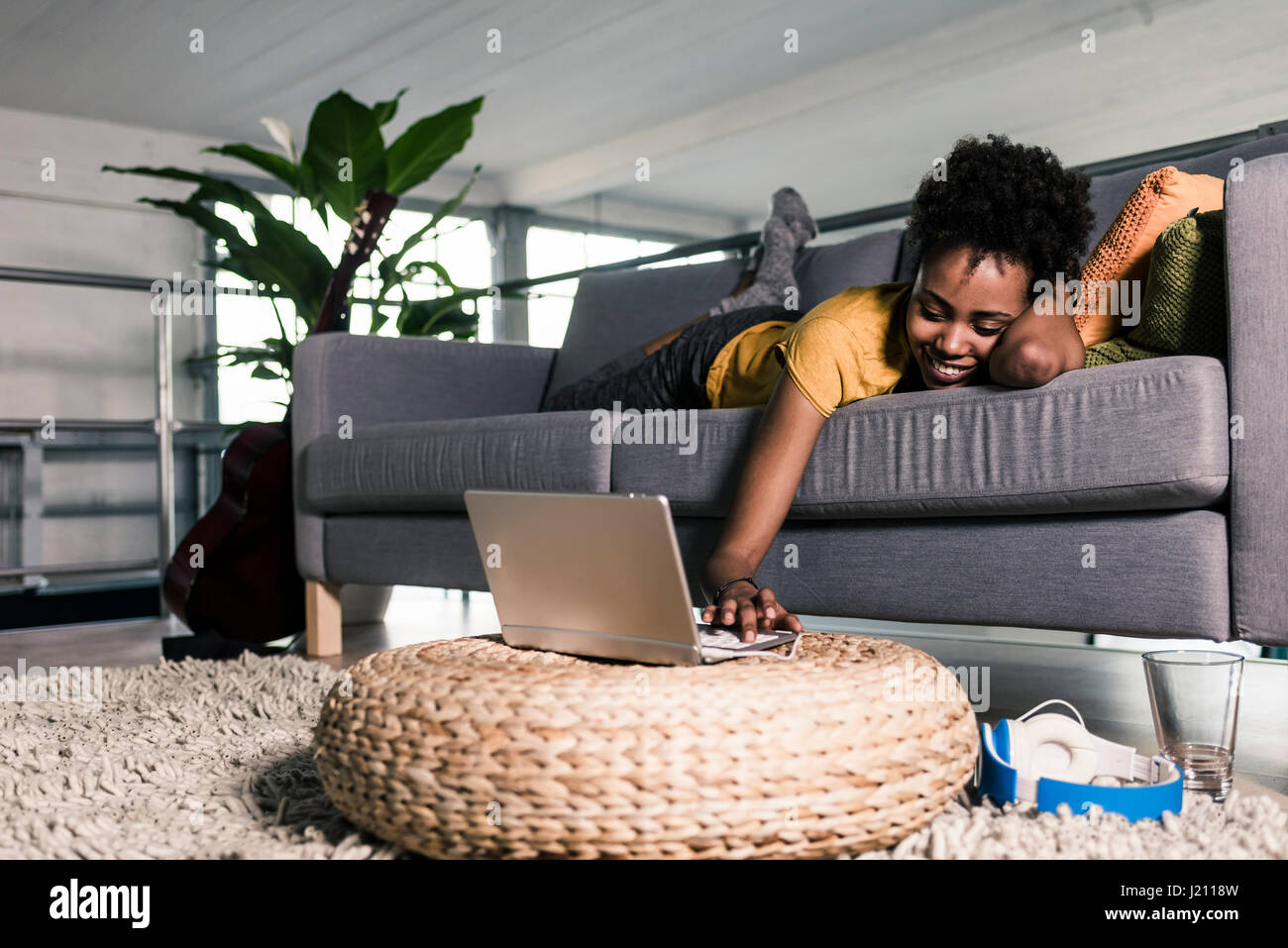 Smiling young woman lying on couch using laptop Stock Photo - Alamy