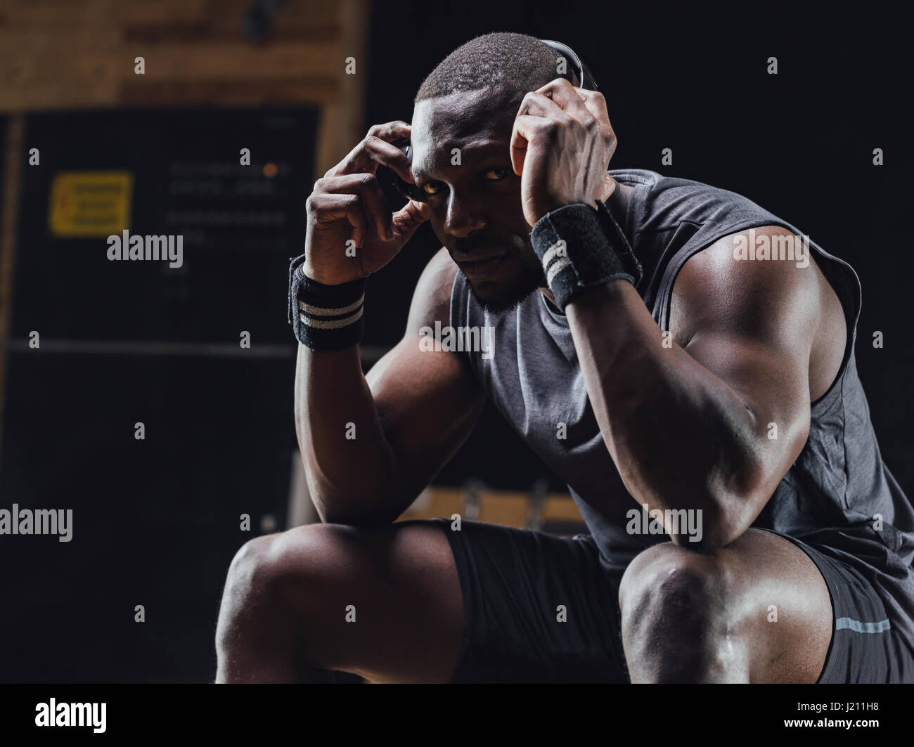 Athlete sitting in gym, wearing headphones, concentrating Stock Photo