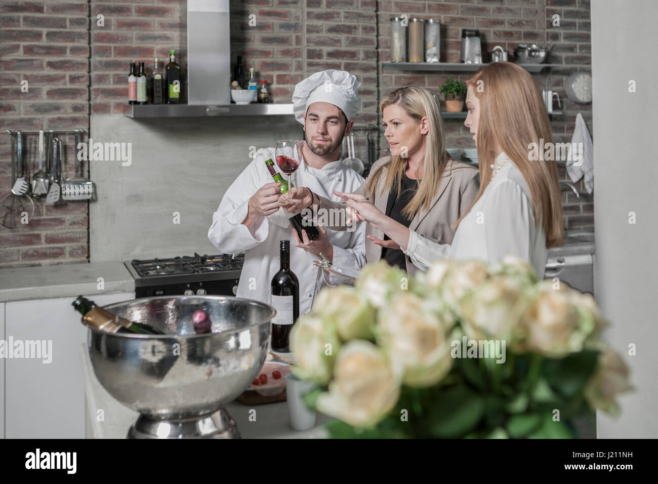 Chef with two women in kitchen tasting wine Stock Photo