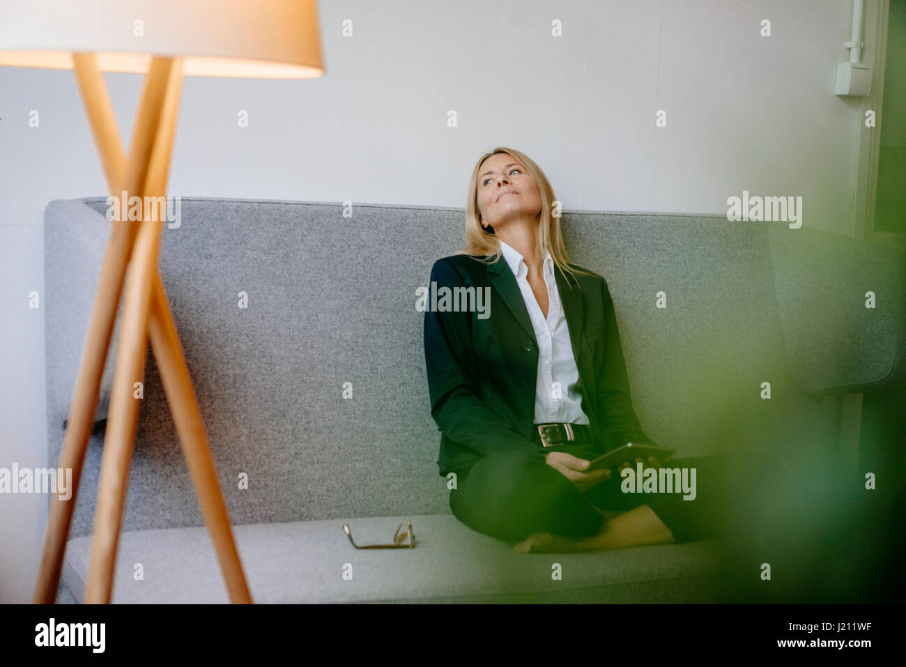 Relaxed businesswoman sitting on couch holding tablet Stock Photo - Alamy