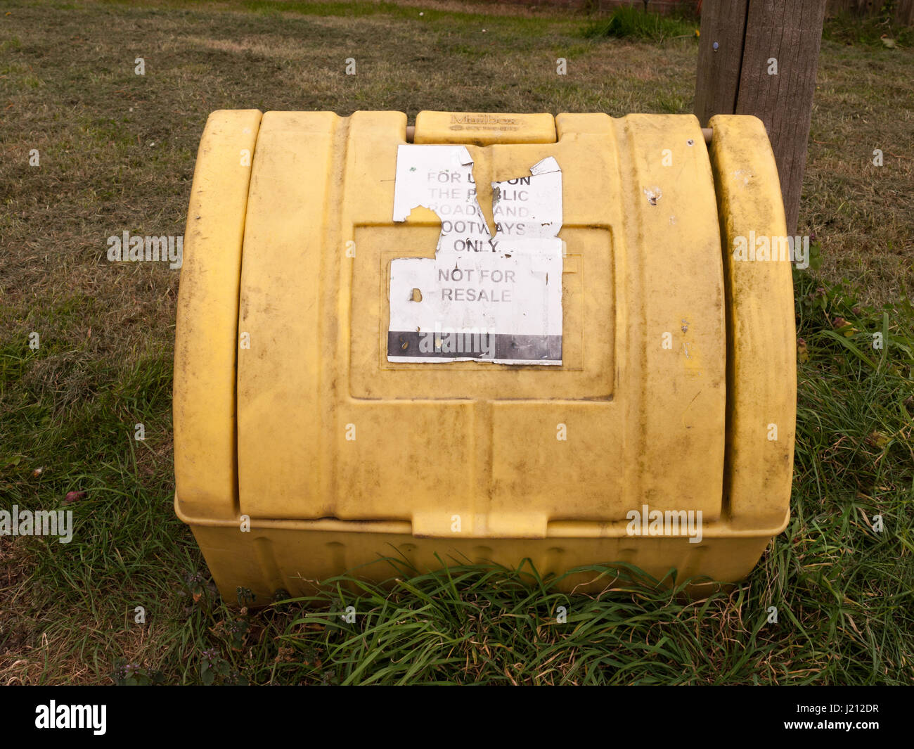 a yellow grit box outside with its lid closed and on the grass next to