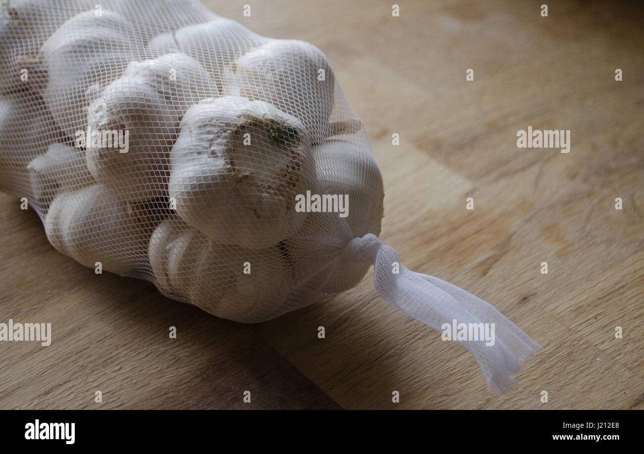 Bunch of garlic in net on wooden bench close up Stock Photo