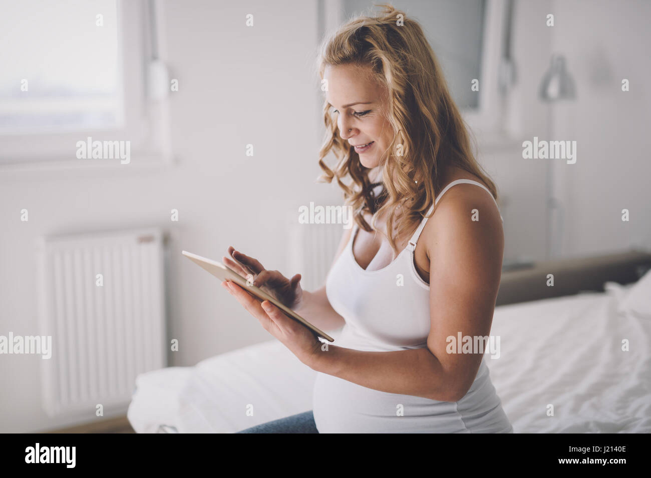 Beautiful expectant pregnant woman using tablet and smiling Stock Photo
