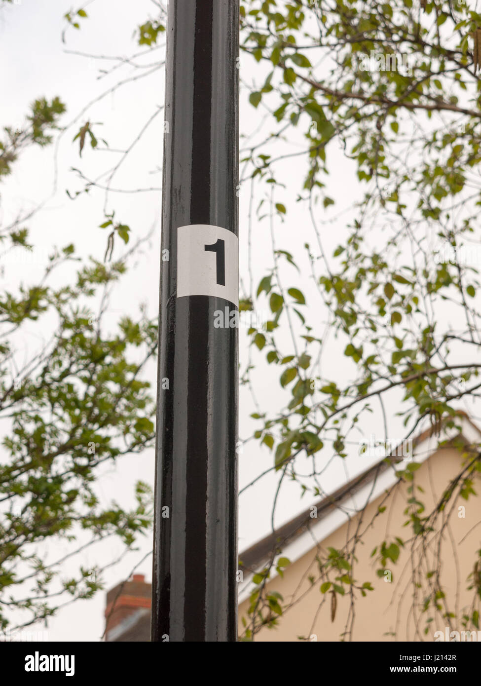 a black pole leading up with a white sticker and the number 1 on it, clear directions numbering one, stuck stamp label labeled england uk suburbs urba Stock Photo
