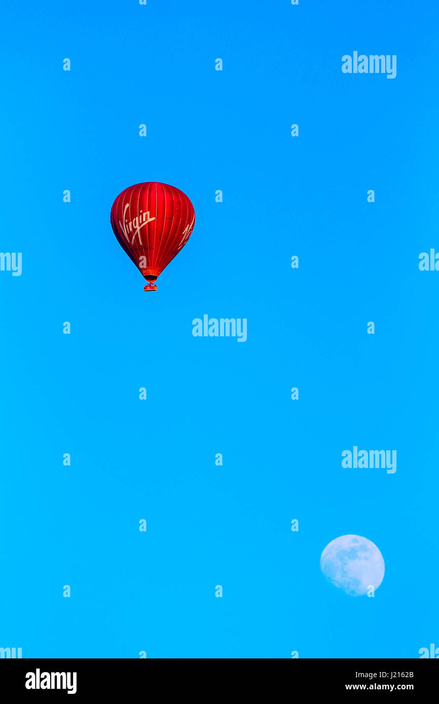 Red Virgin hot air balloon flying past the moon with a blue sky background Stock Photo
