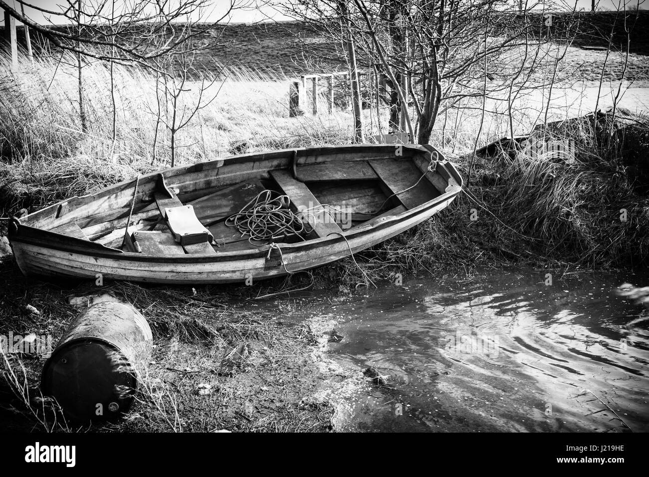 old row boat aground with oil or chemical contaner on it's side in the foreground Stock Photo
