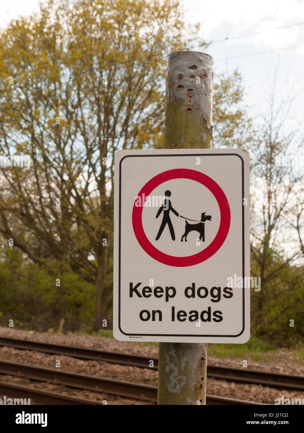 A Railway Safety Sign Saying Keep Dogs on Leads in White and Red and Black on a Pole with