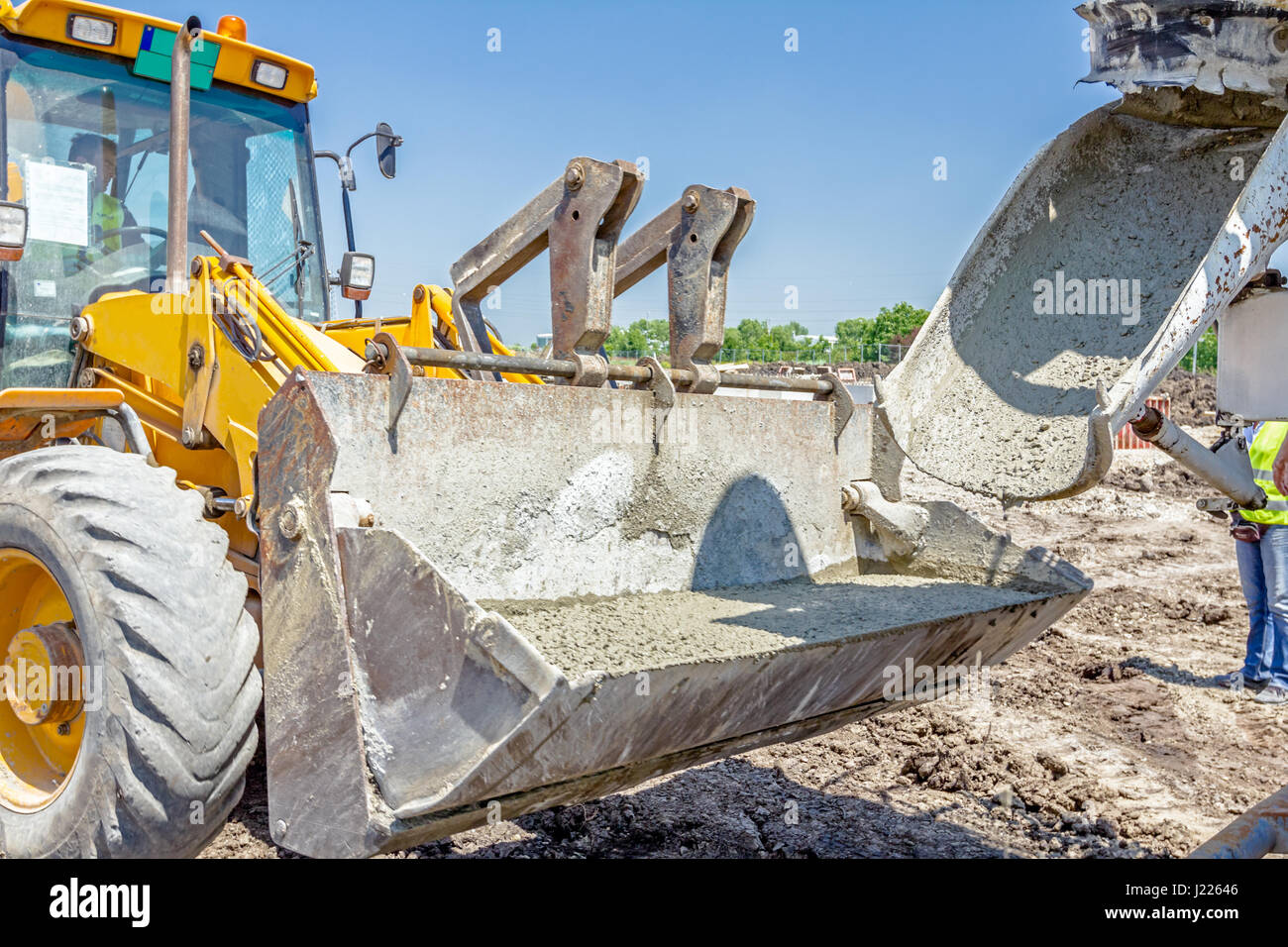 Concrete mixer truck is pouring fresh concrete into excavator bucket at