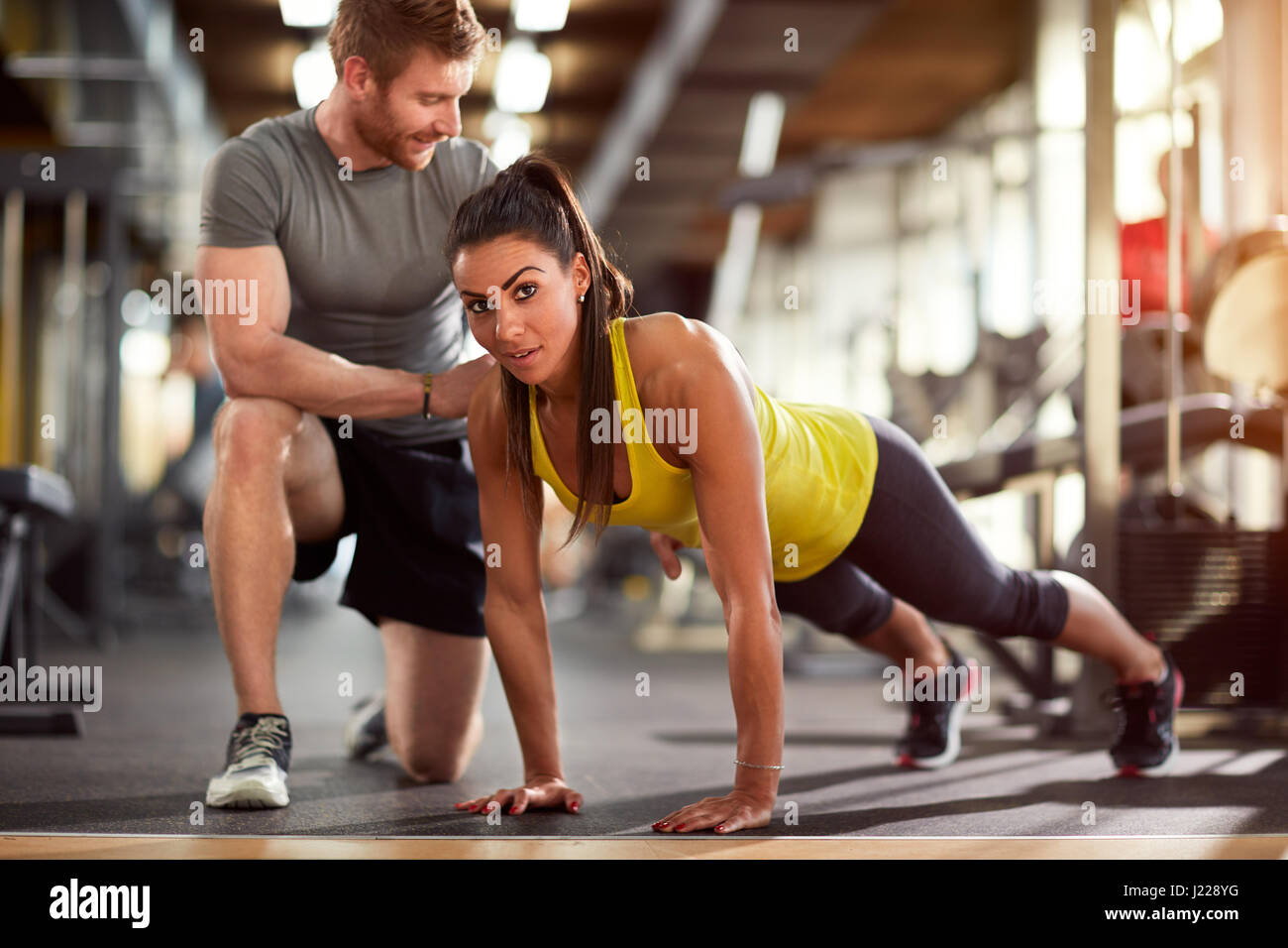 Girl doing pushups with trainer's helps in fitness club Stock Photo