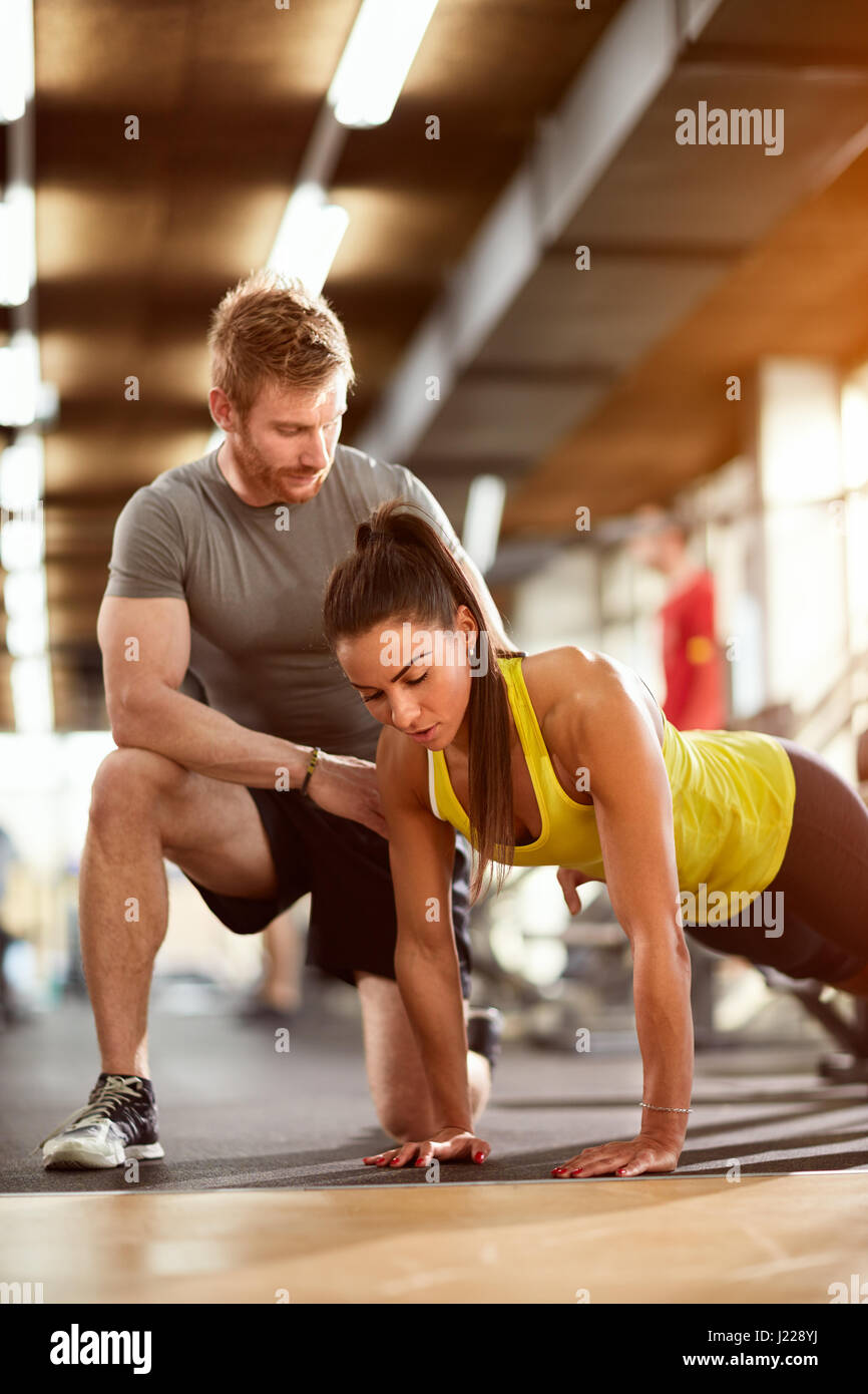 Woman doing pushups with man's assist in fitness club Stock Photo