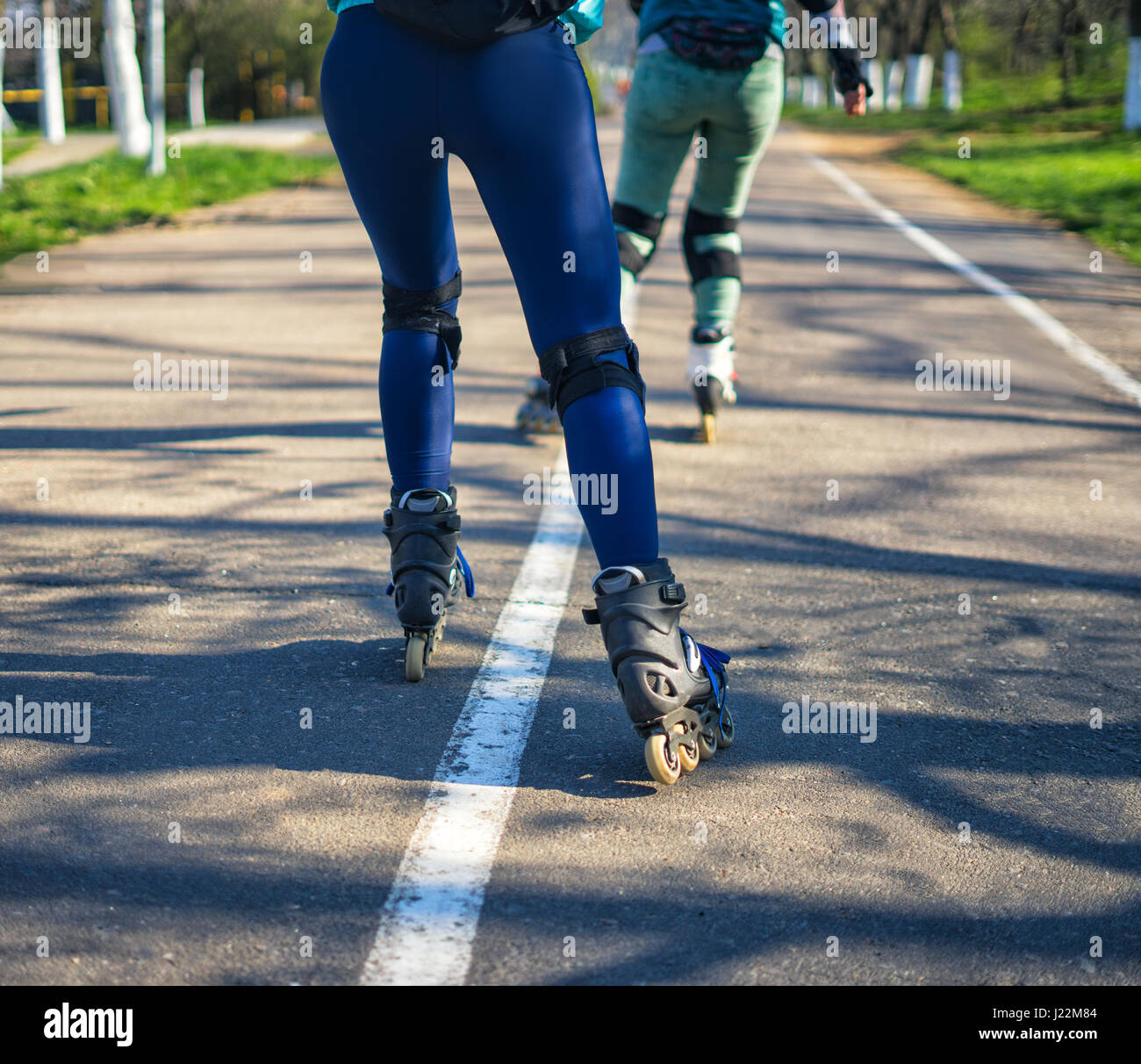 Two girls on roller skates ride along the road next to each other Stock Photo