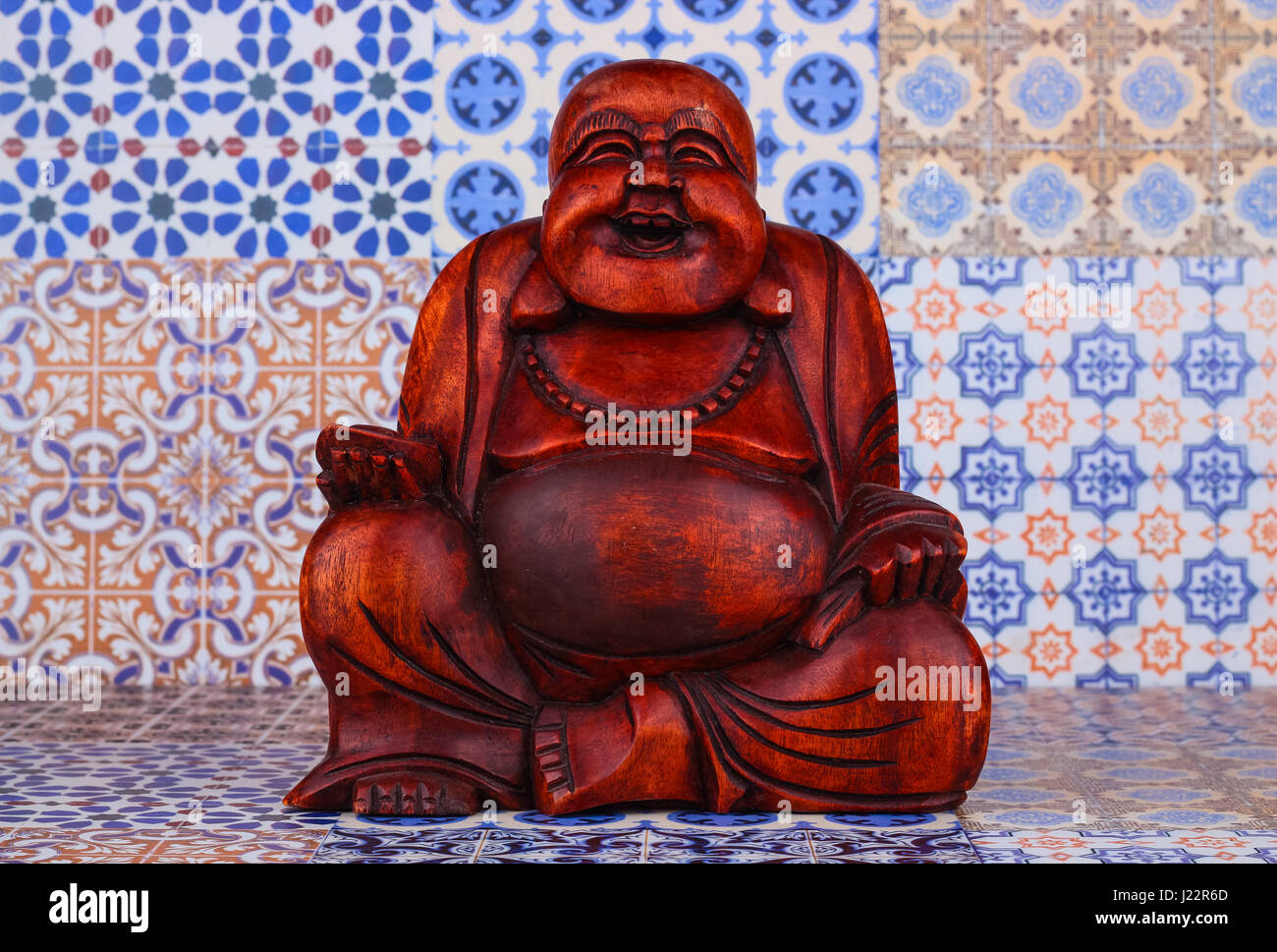 Buddha statue on a colorful background / featuring a wooden statue of  cheerful wise Buddha on colorful Oriental artistic pattern background Stock Photo