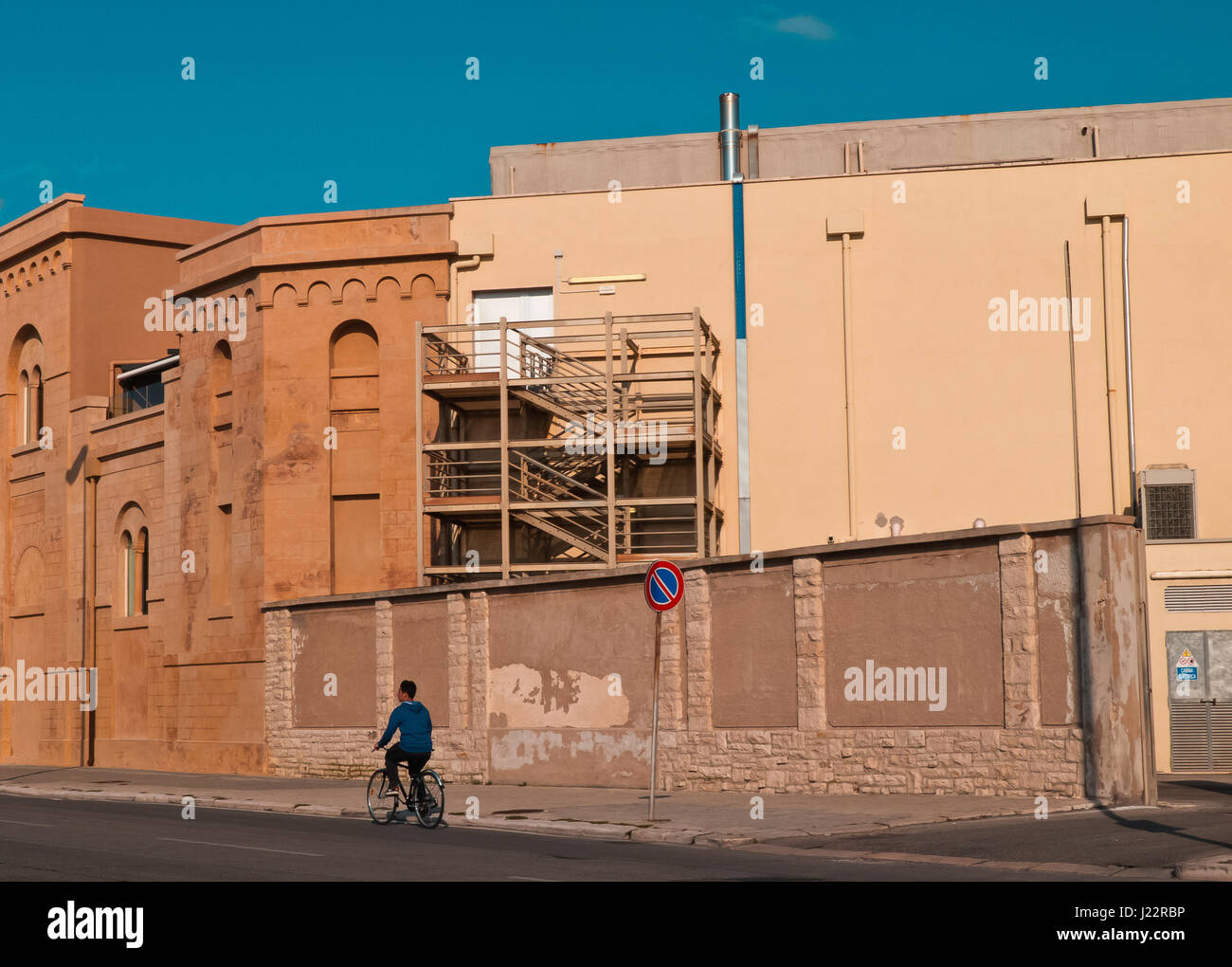 Boy on bicycle who crossing near factory facade in the Bari city. Stock Photo