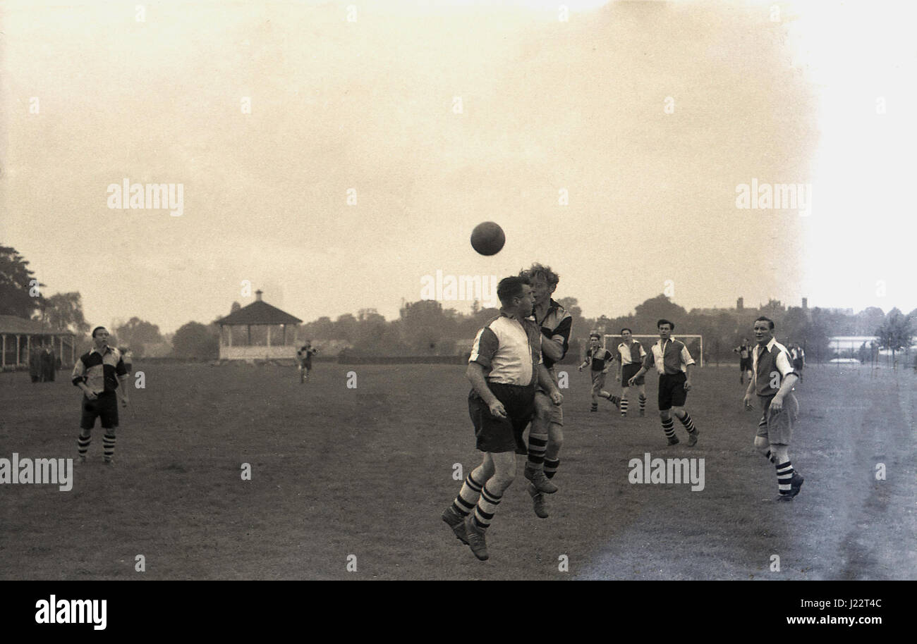 1950s, an amateur football match, two footballers in long baggy shorts and ankle high leather boots compete for the ball in the air, England. UK. Stock Photo