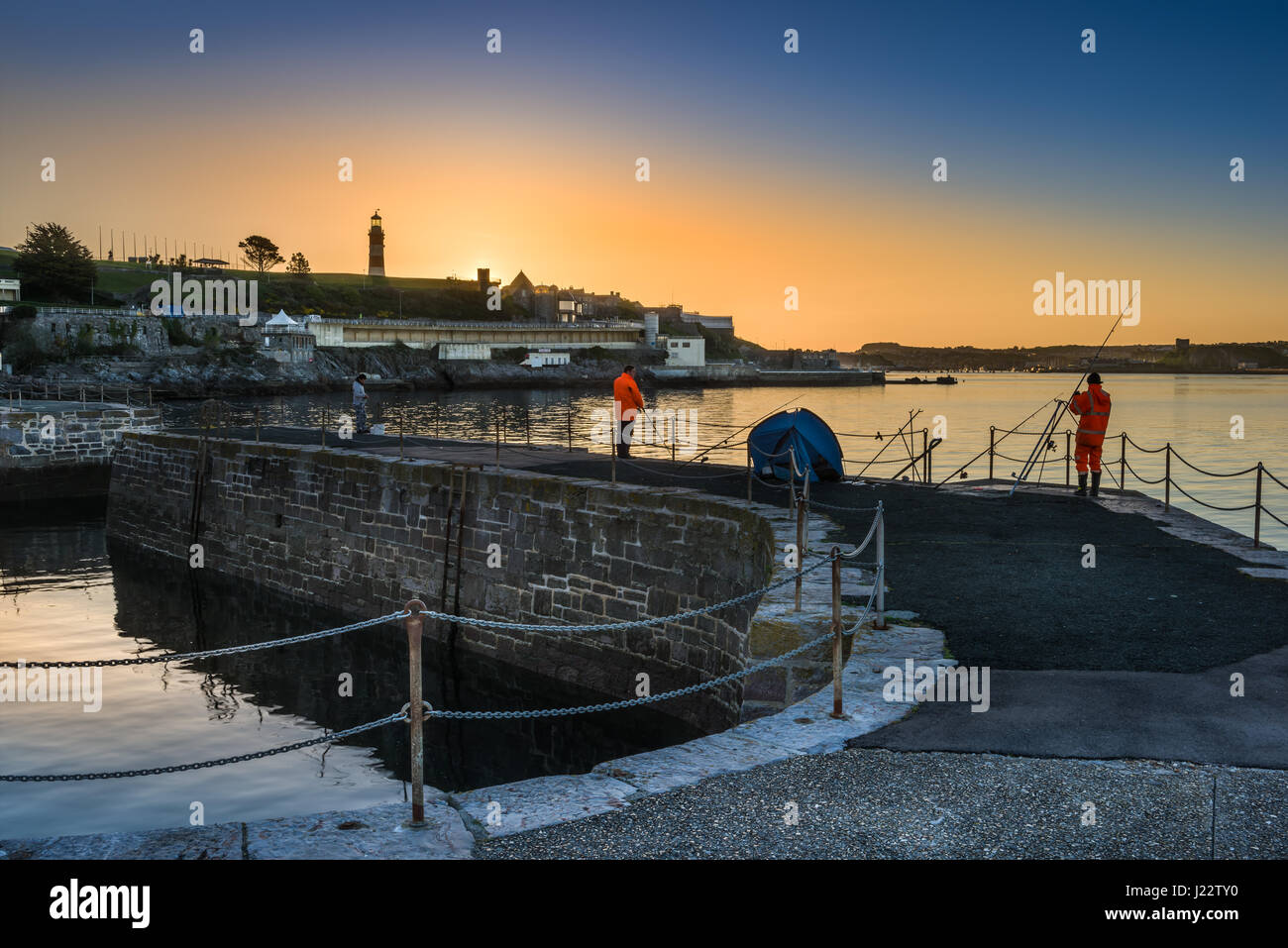 Anglers are treated to a golden sunrise on the Waterfront Harbour as the sun rises behind Smeatons Tower in Plymouth, Devon. Stock Photo