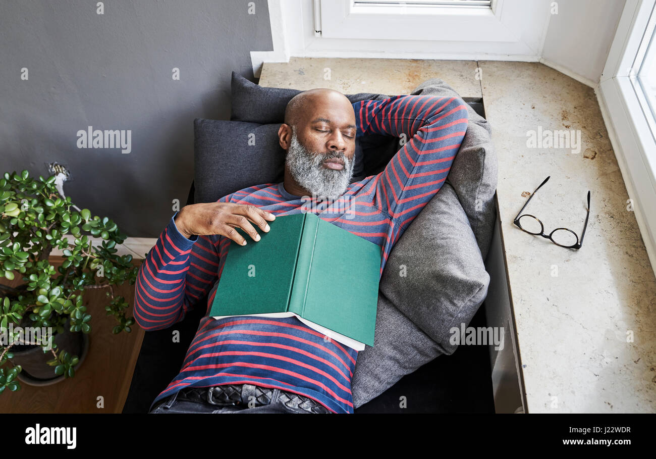 Matur man lying on bench with a book, taking a nap Stock Photo