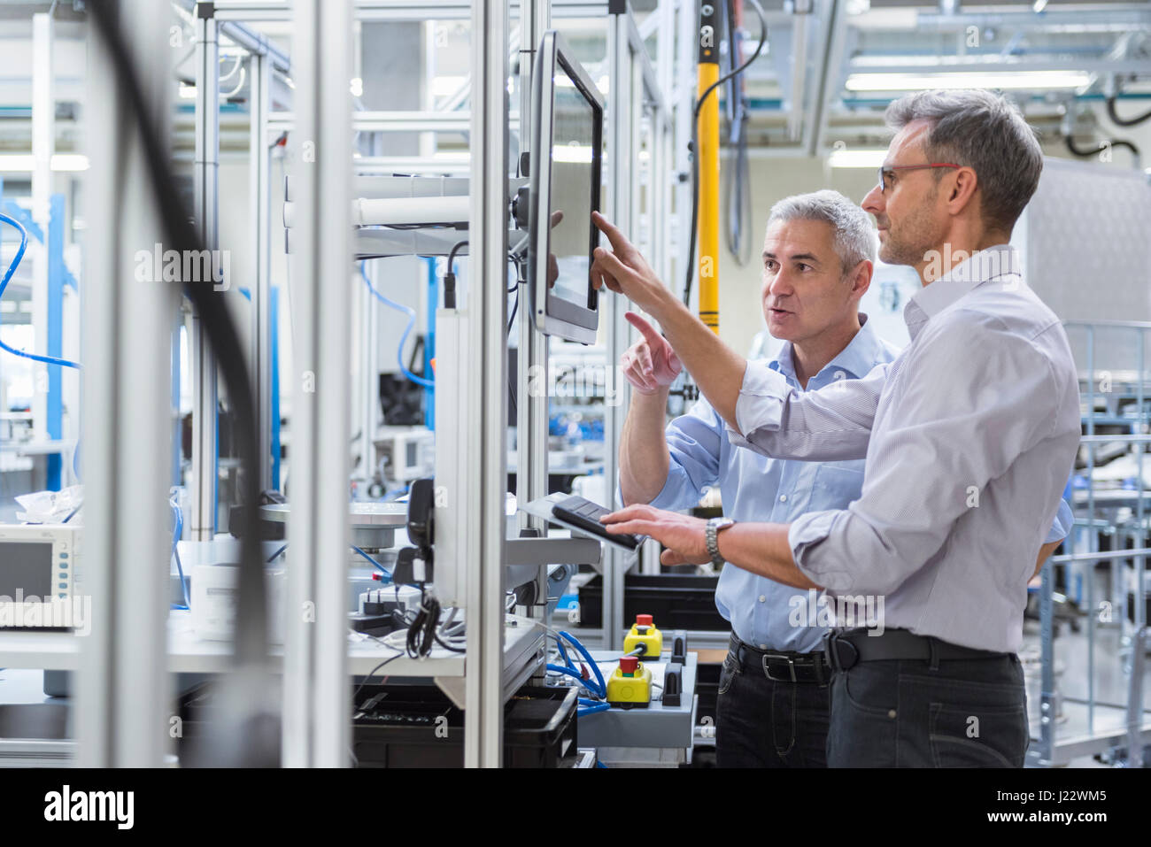 Two businessmen in modern factory hall talking at computer monitor Stock Photo