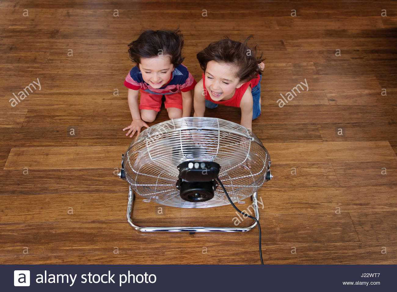 Twin Brothers Kneeling On Wooden Floor In Front Of Fan Having Fun