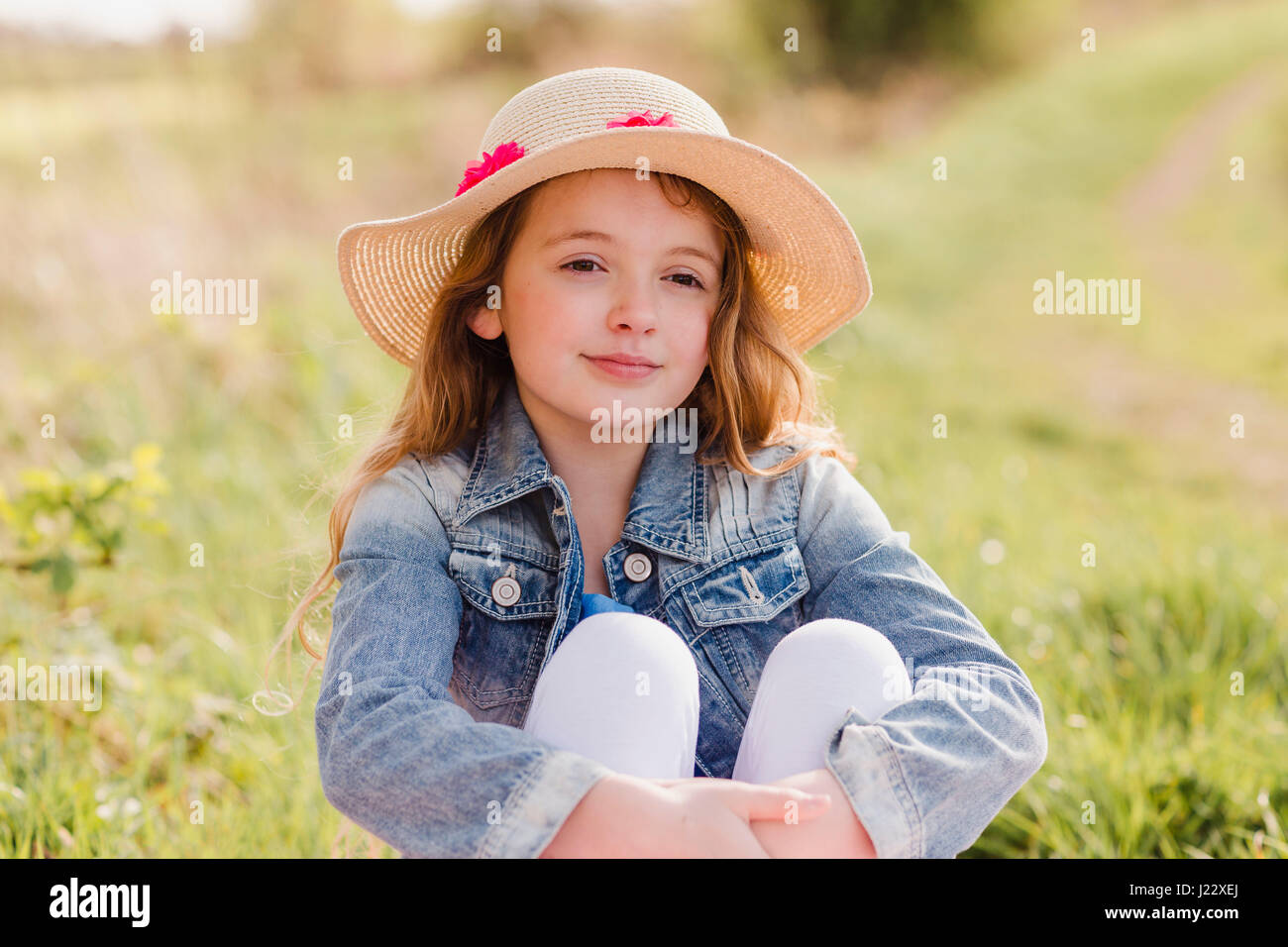 Portrait of girl wearing straw hat sitting on a meadow Stock Photo - Alamy