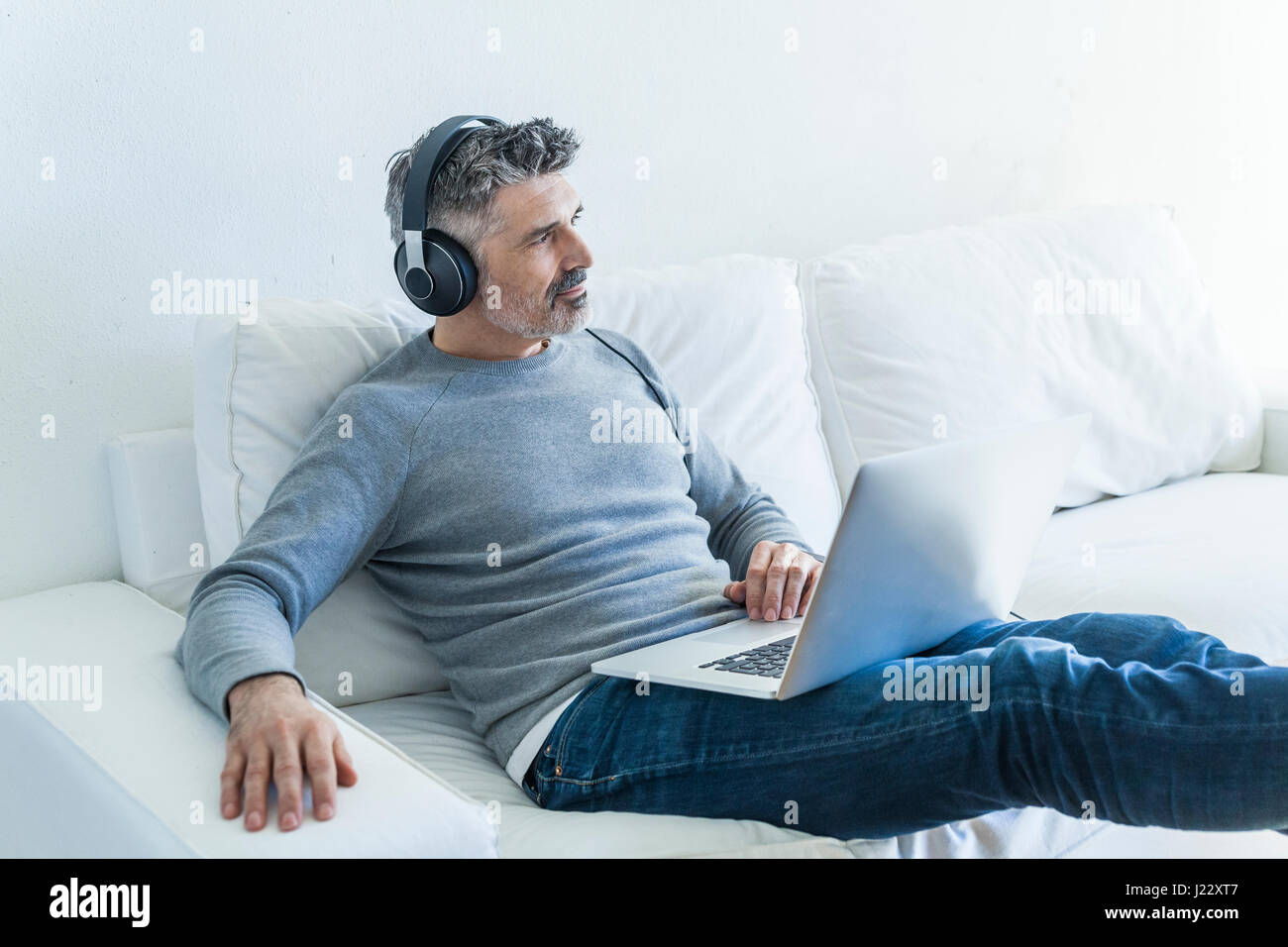 Mature man at home using laptop and wearing headphones Stock Photo - Alamy