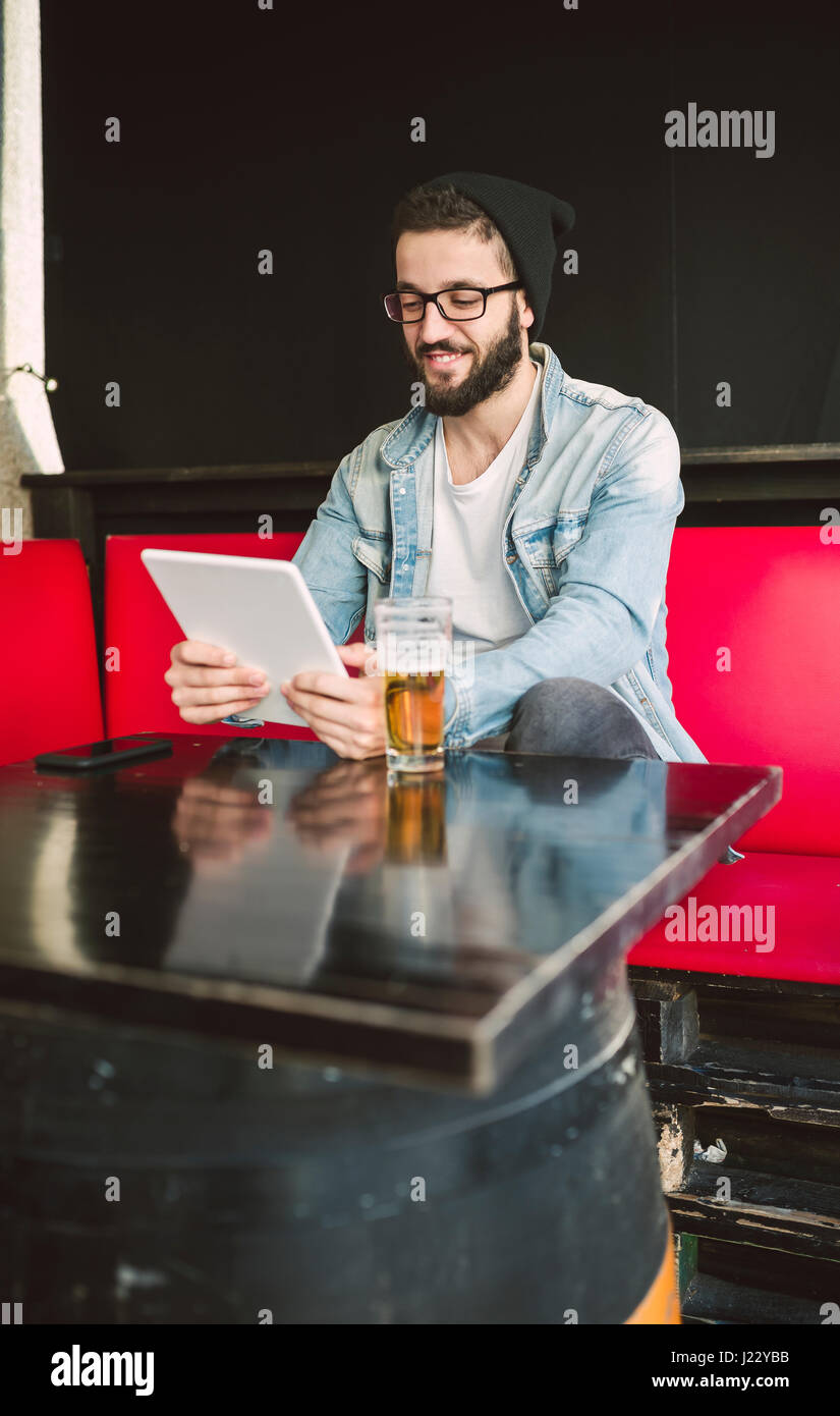 Smiling young man sitting in a pub using tablet Stock Photo