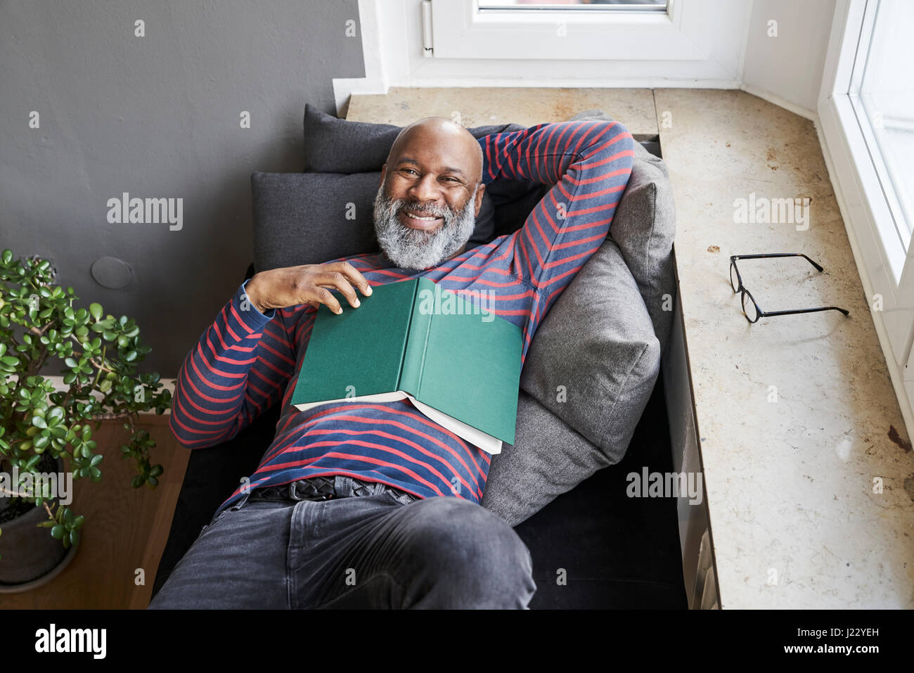 Matur man lying on bench with a book, smiling Stock Photo