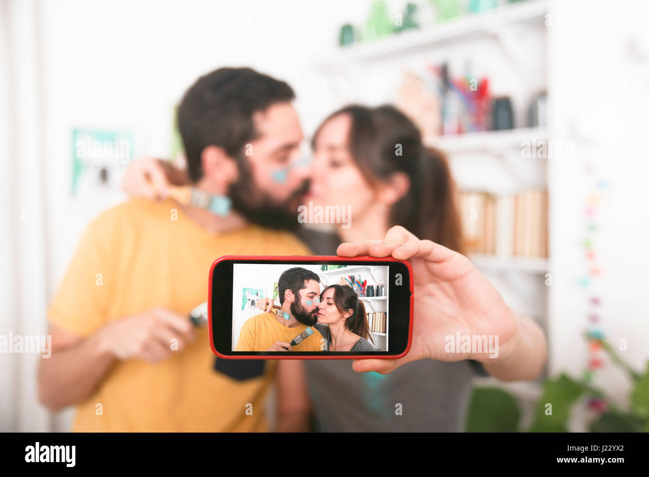 Young couple kissing and taking a selfie with paintbrushes Stock Photo