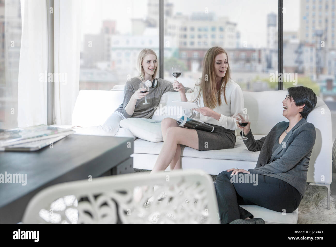 Happy friends with red wine socializing in city apartment Stock Photo