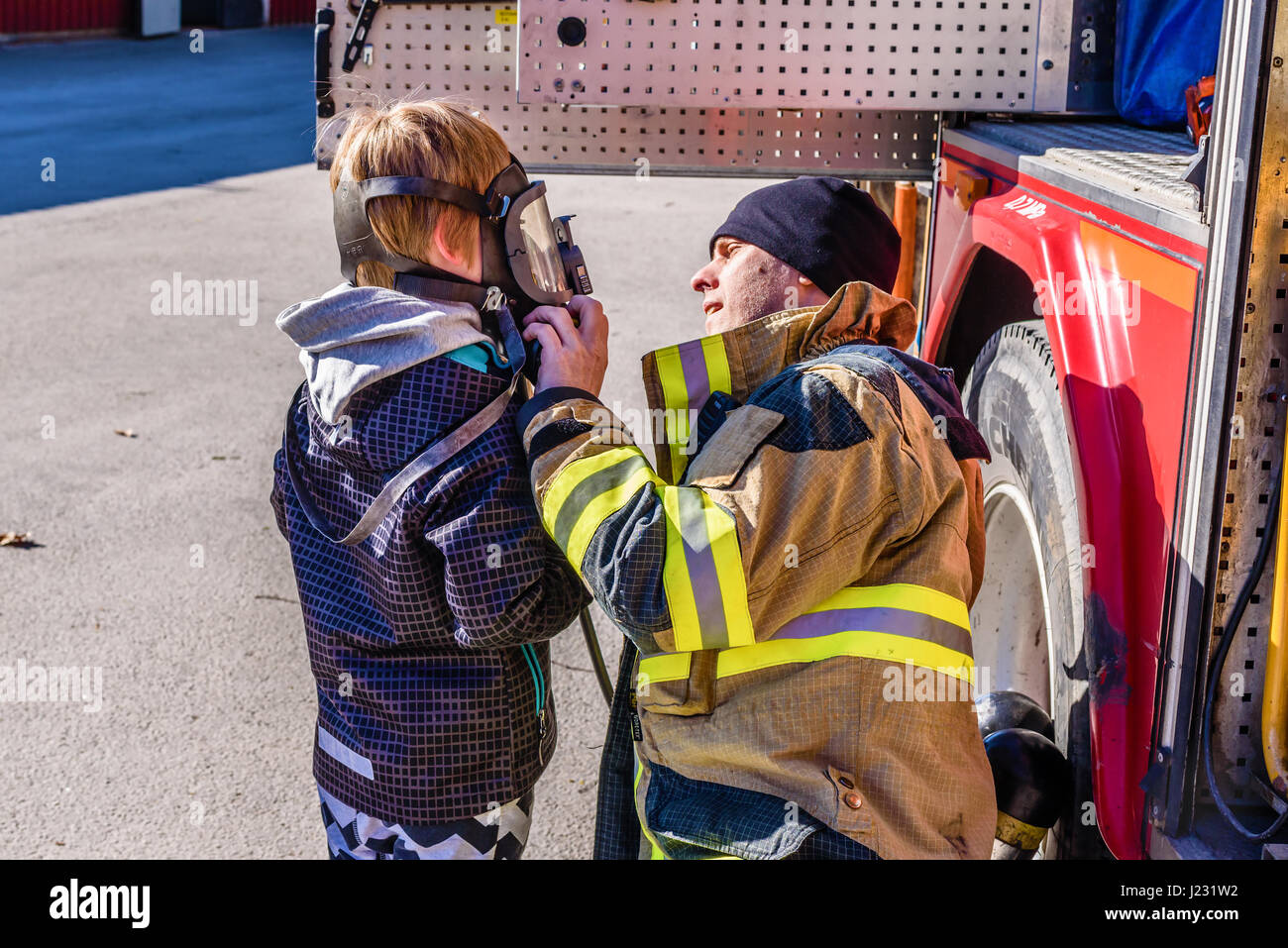 Brakne Hoby, Sweden - April 22, 2017: Documentary of public fire truck presentation. Firefighter helping young boy try a self-contained breathing appa Stock Photo