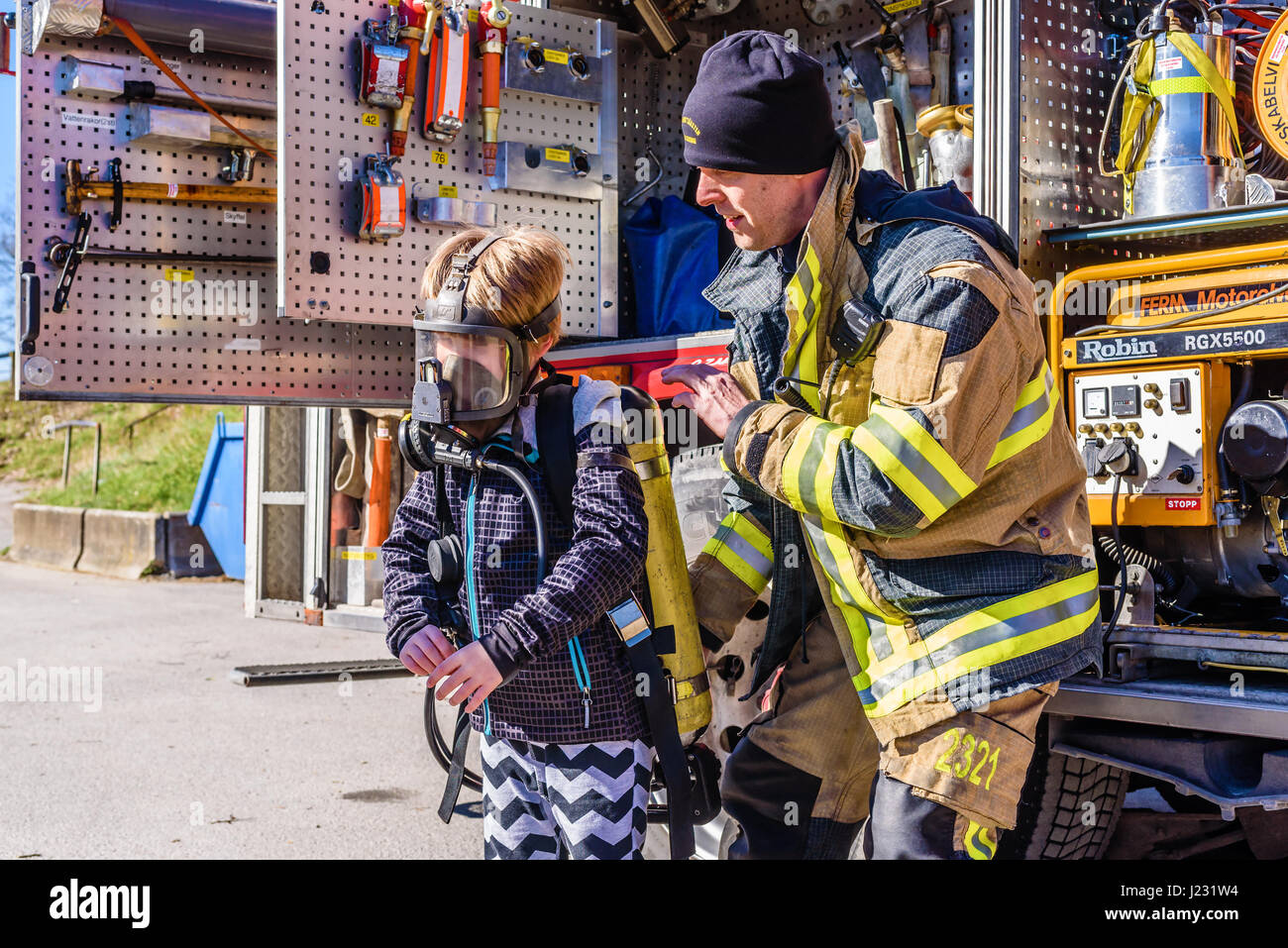 Brakne Hoby, Sweden - April 22, 2017: Documentary of public fire truck presentation. Firefighter helping young boy try a self-contained breathing appa Stock Photo