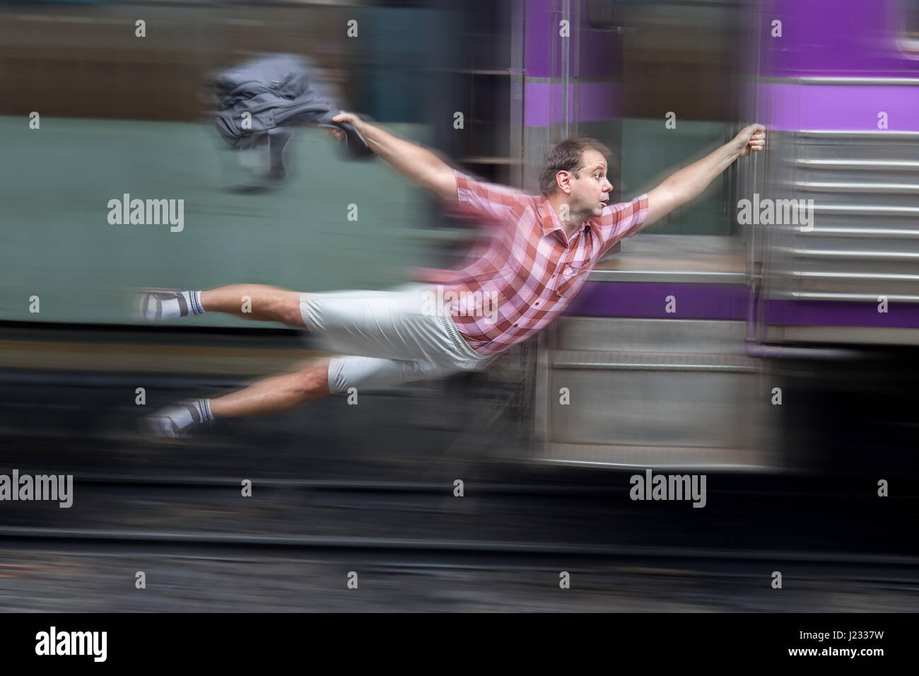 Man with backpack flies behind a moving train. Tourist holding a moving train from a railway station. Funny traveler catches the train in motion. Stock Photo