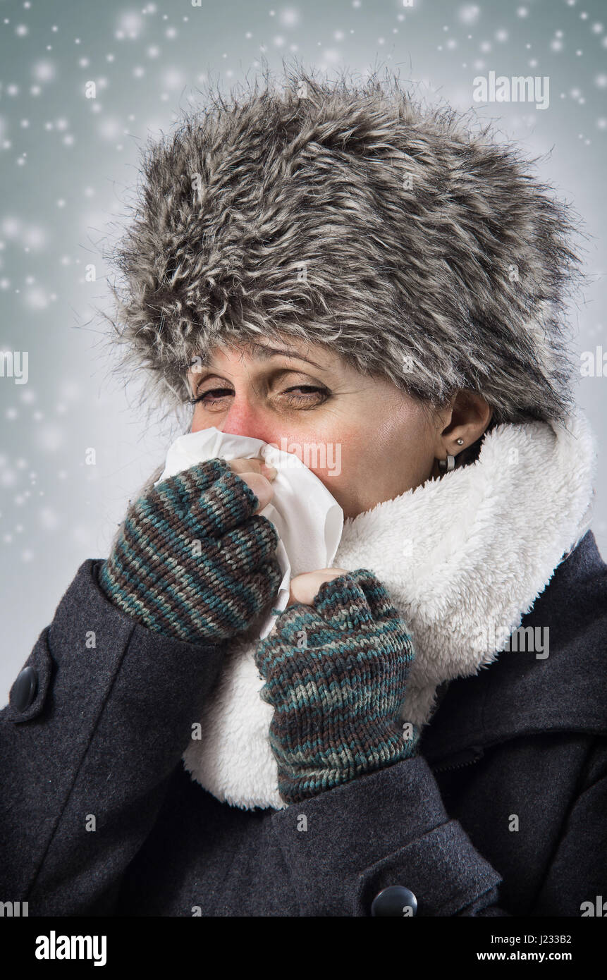 Ill woman with warm clothes blowing her nose under snow fall Stock Photo
