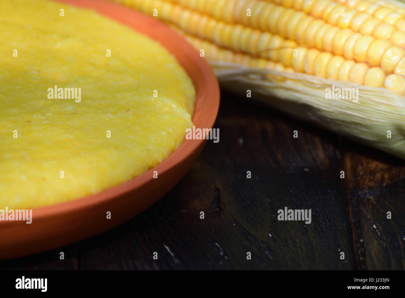 Close shoot of corn porridge on clay plate next to a corn cob. Wooden table, outdoors. Stock Photo
