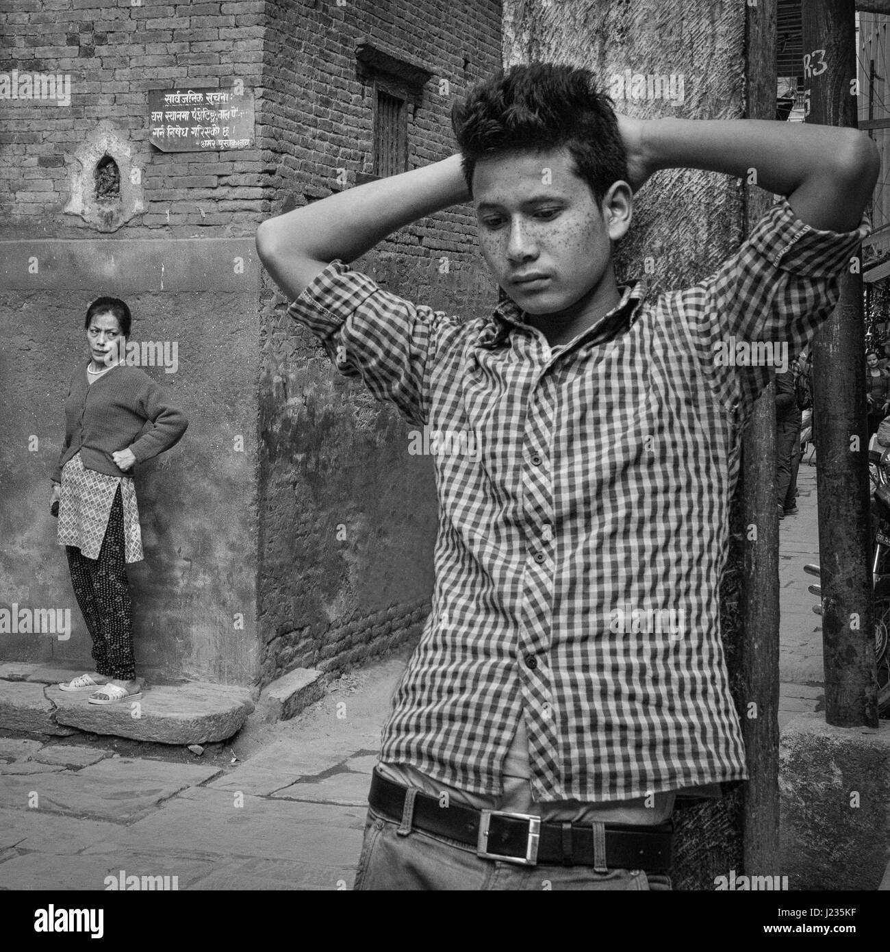 Teenage boy standing on the street as woman looks on in Patan, Nepal. Stock Photo