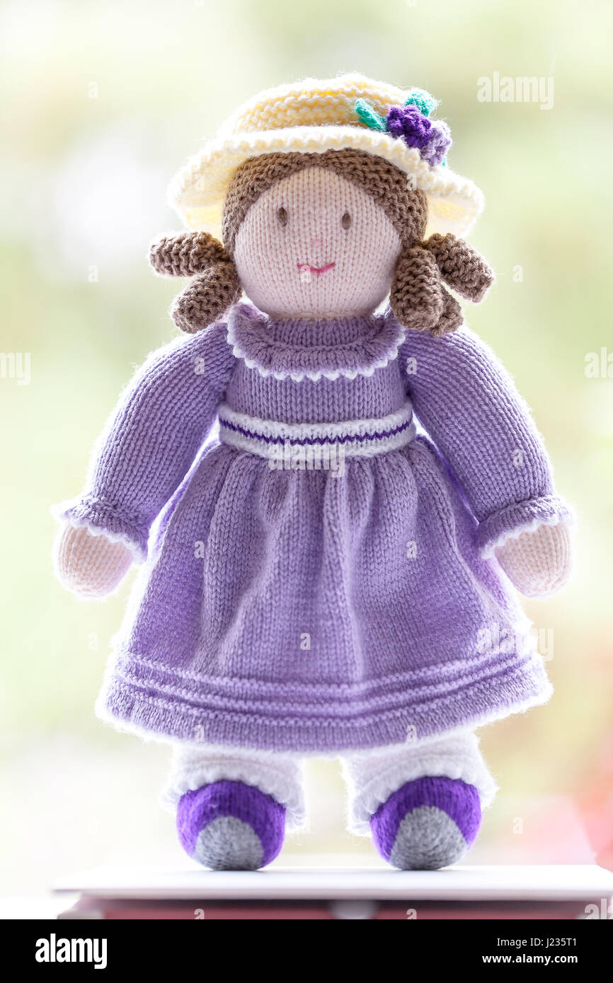 Handmade knitted wool doll with pigtails wearing a pretty lilac purple  dress with a hat and grey booties against a soft blurred green background.  Nice Stock Photo - Alamy