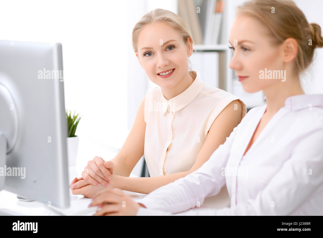 Two business women sitting at the desk in office Stock Photo - Alamy