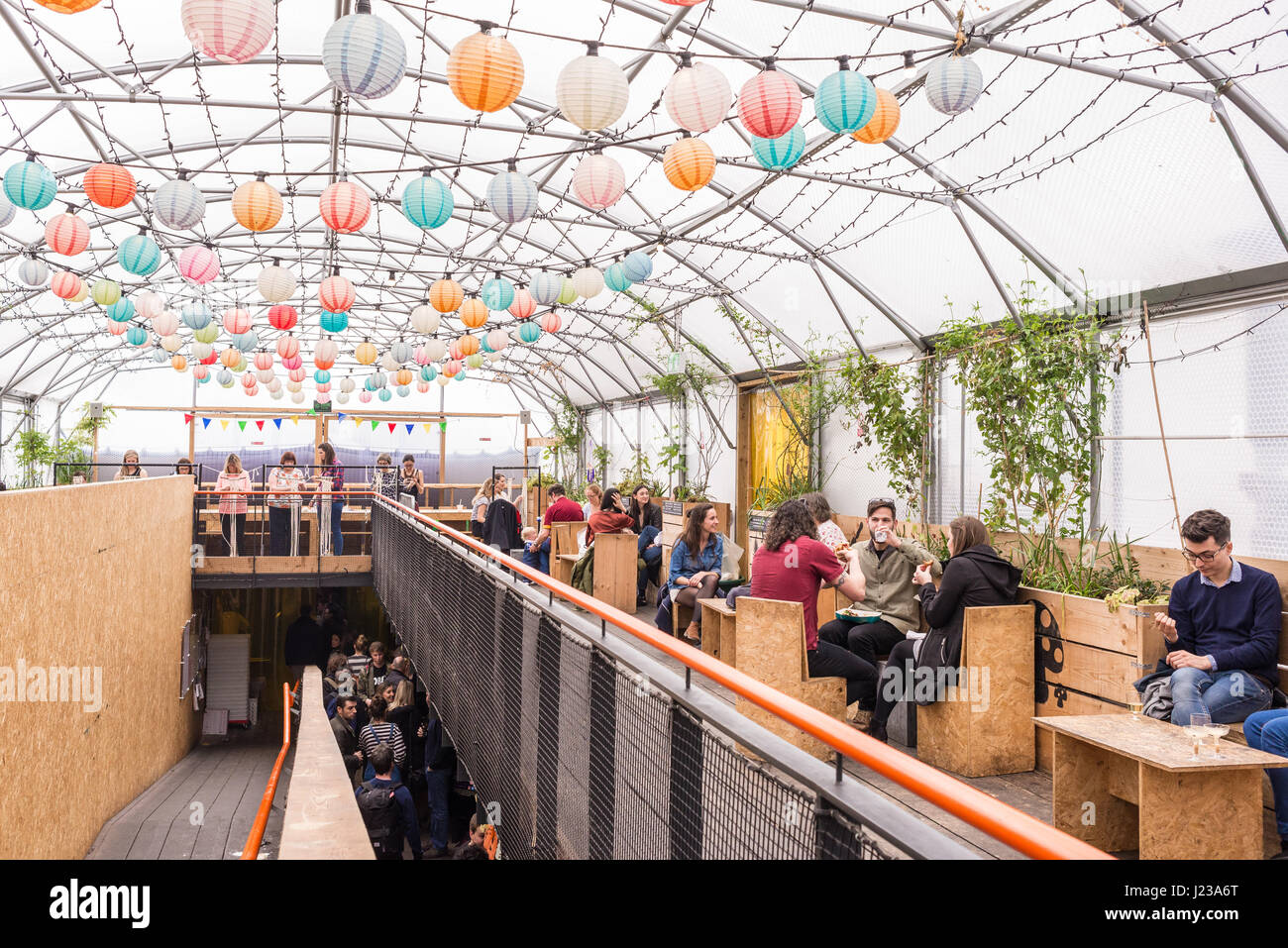 People eating and drinking in the The Greenhouse, a large covered polytunnel in Pop Brixton.Pop Brixton is an event venue and the home of a community  Stock Photo