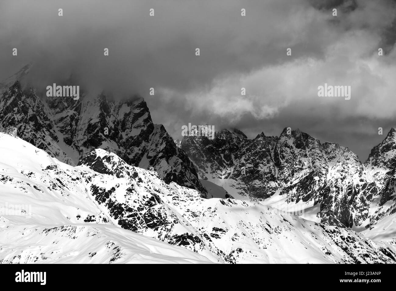 Black and white snowy rocks in clouds at sunny day. Caucasus Mountains. Georgia, region Svaneti. Stock Photo