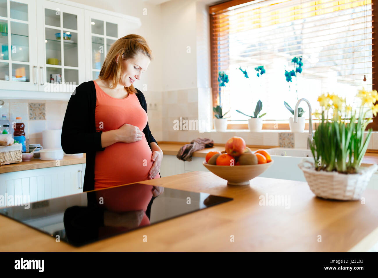 Beautiful pregnant woman in kitchen holding her belly Stock Photo