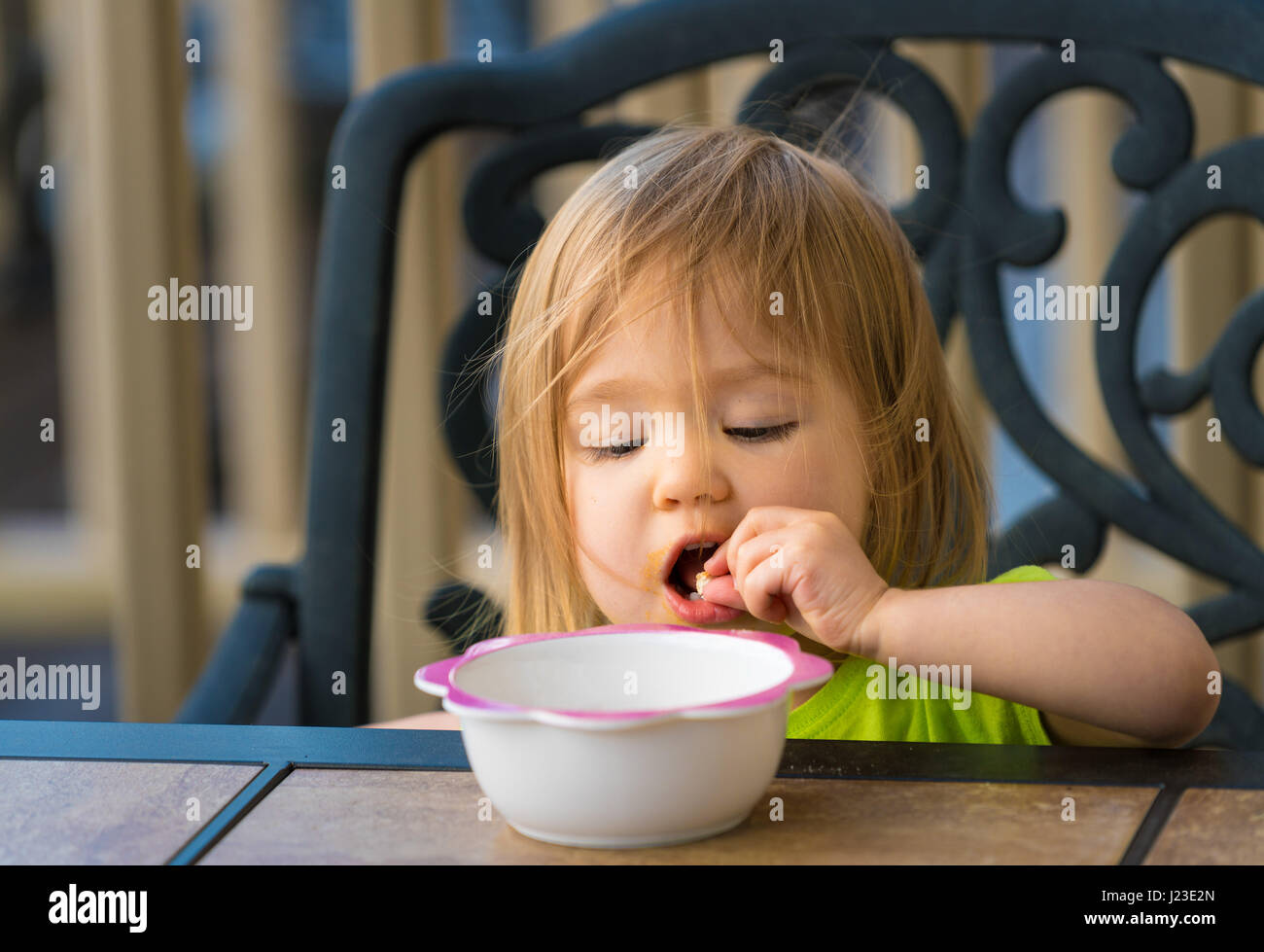 Baby girl, toddler child eating with hands and fingers from bowl on outdoor table Stock Photo
