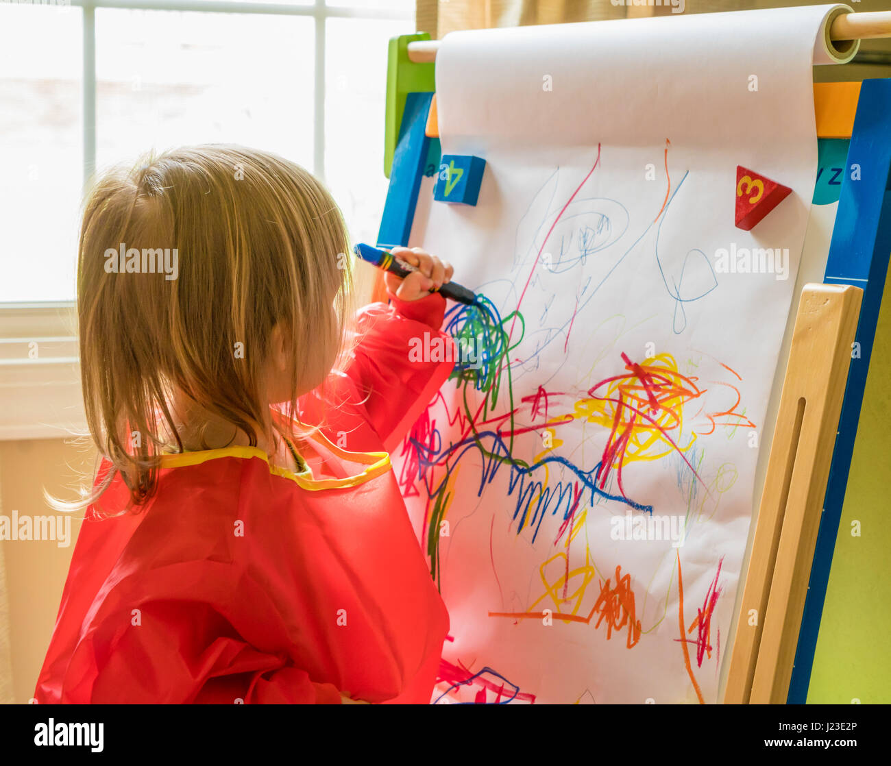 Young child drawing with crayon left handed on an easel during nursery playtime Stock Photo