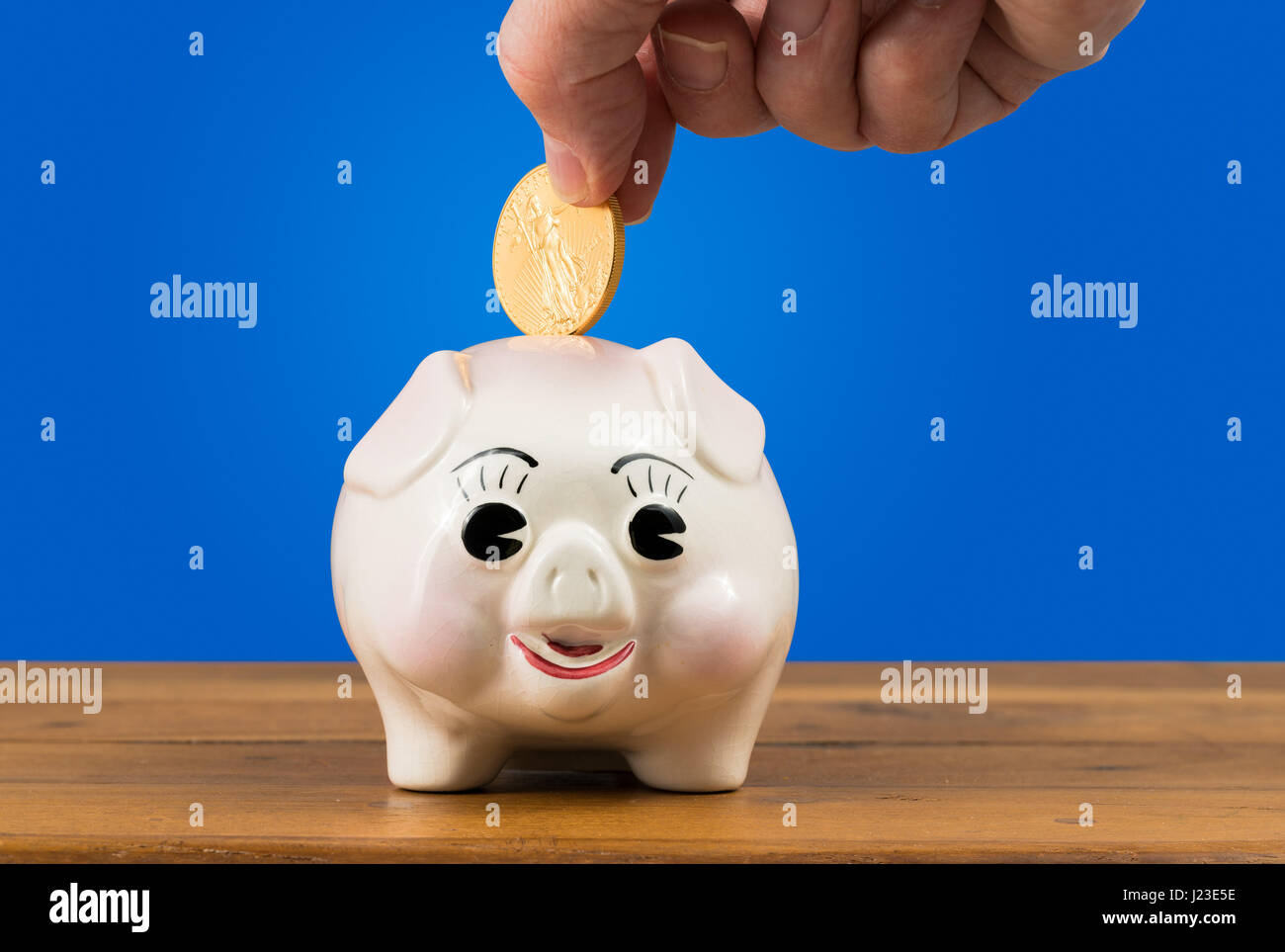 Piggy bank with a hand putting a gold coin in - savings or investment concept Stock Photo